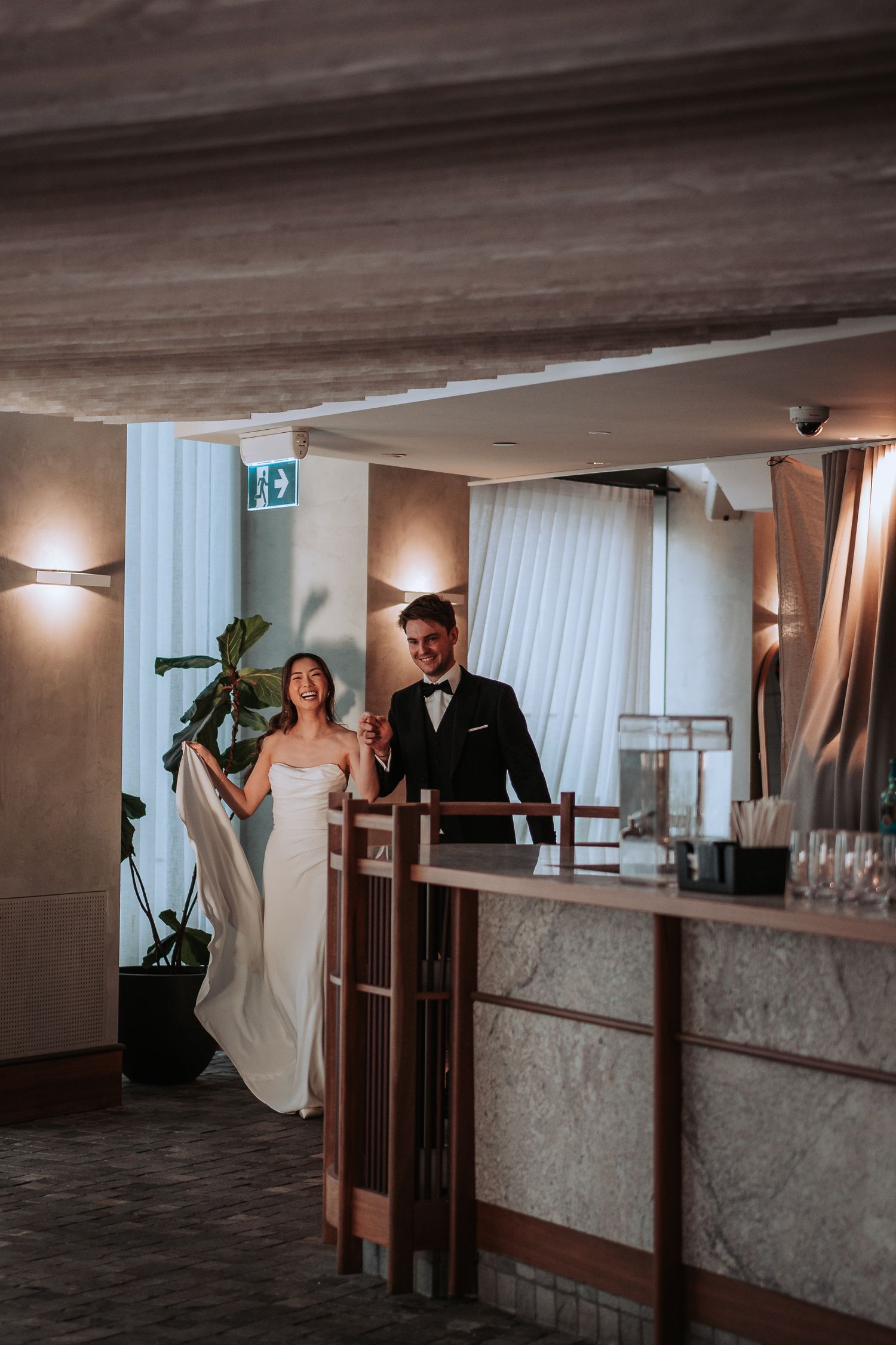 Couple poses together at modern wedding venue with decorative bar and lighting.