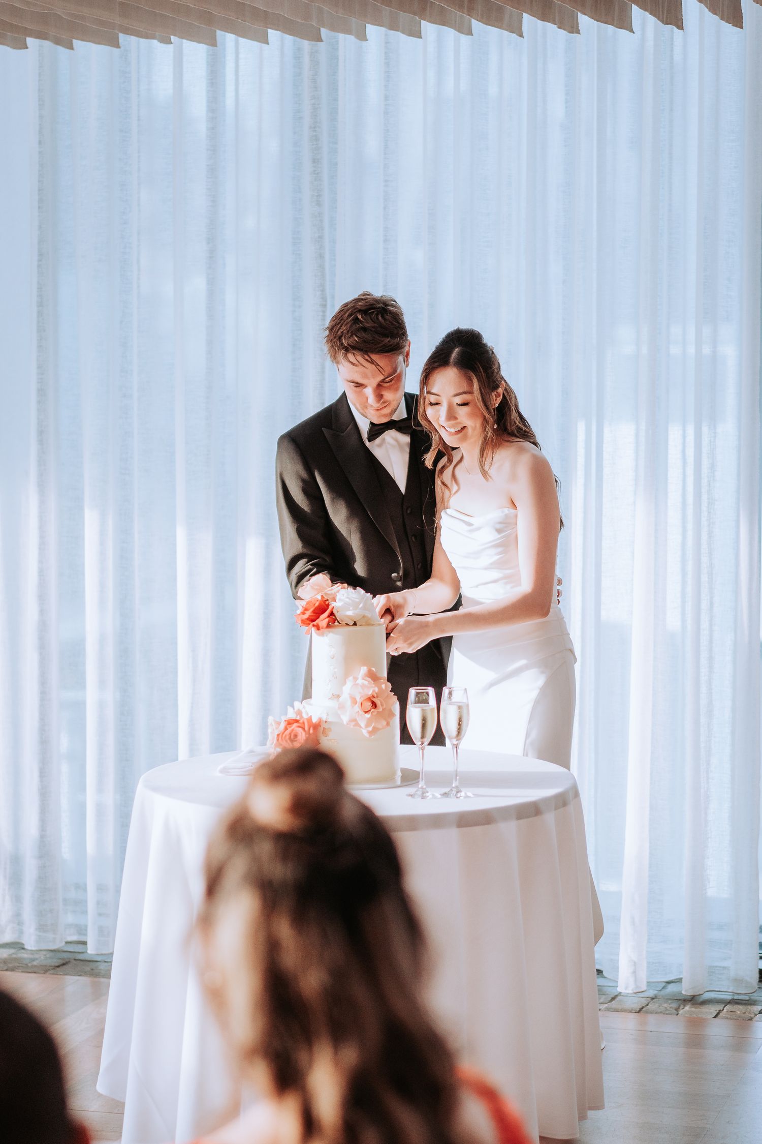 Couple cuts their wedding cake together at an elegant reception with white decor.