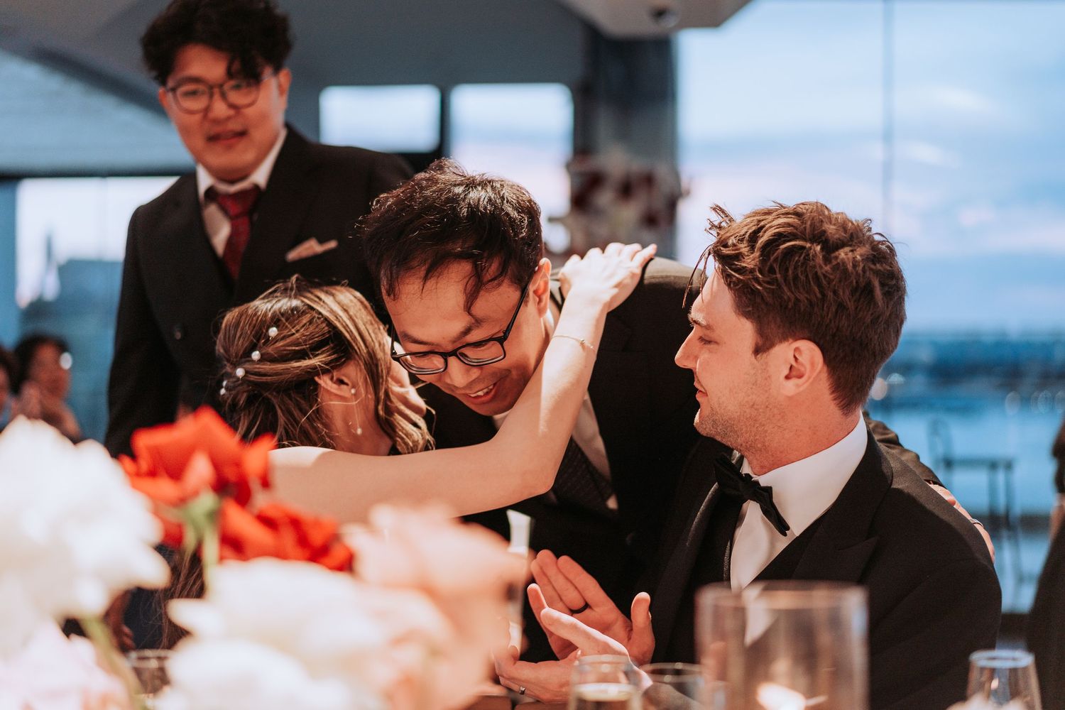Wedding guests interact warmly during dinner at a celebratory reception with floral decorations.