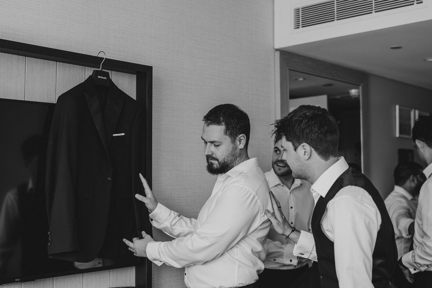 Black and white photo of people getting dressed in formal attire in hotel room.
