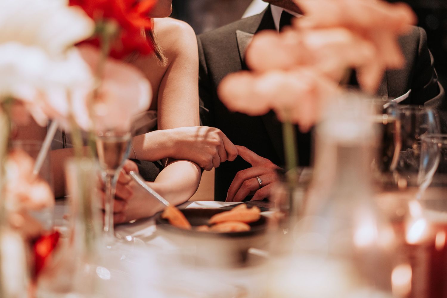 Close-up of hands during an intimate wedding reception moment with soft floral decor.