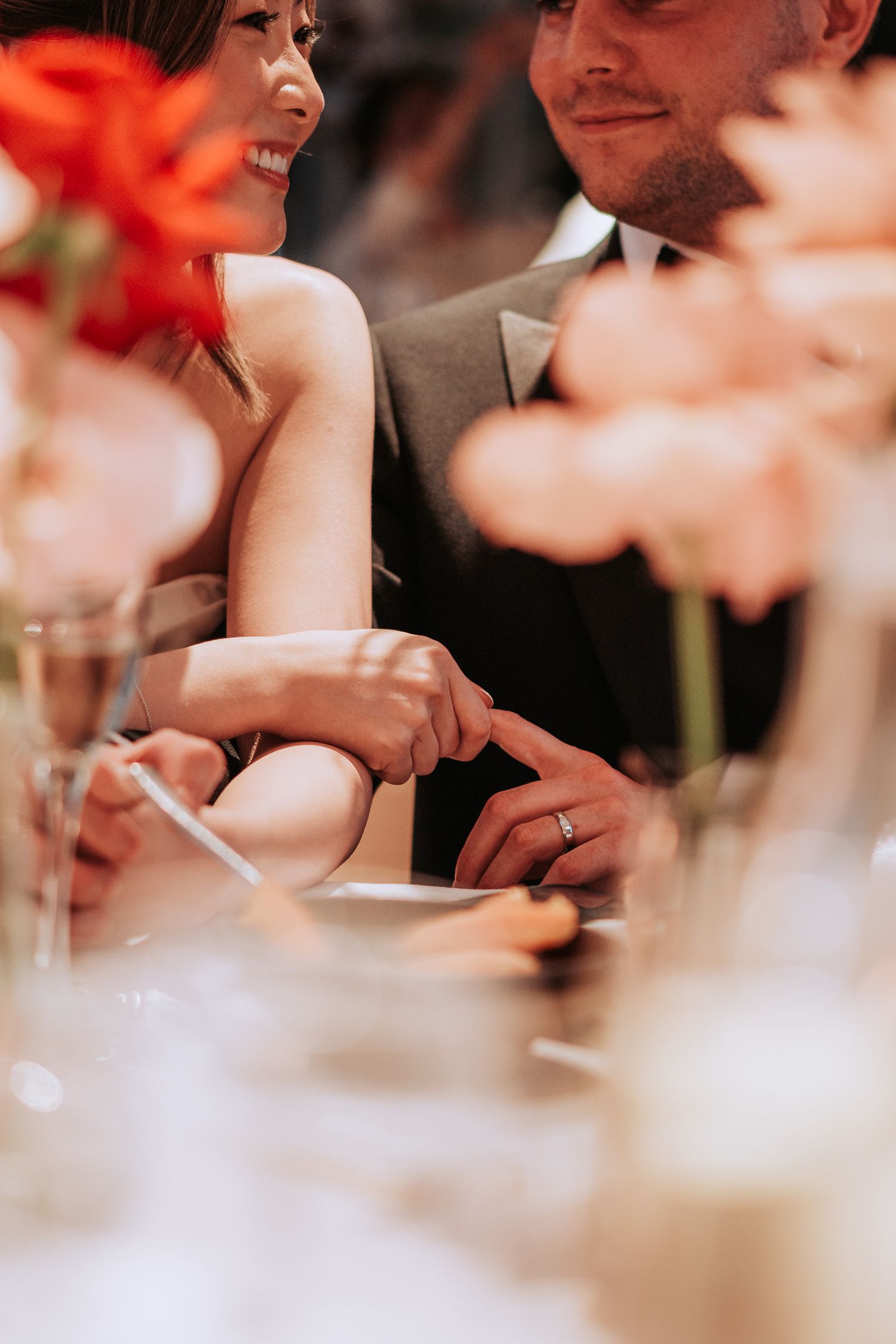 Couple shares an intimate moment at their reception table with coral flowers in foreground.