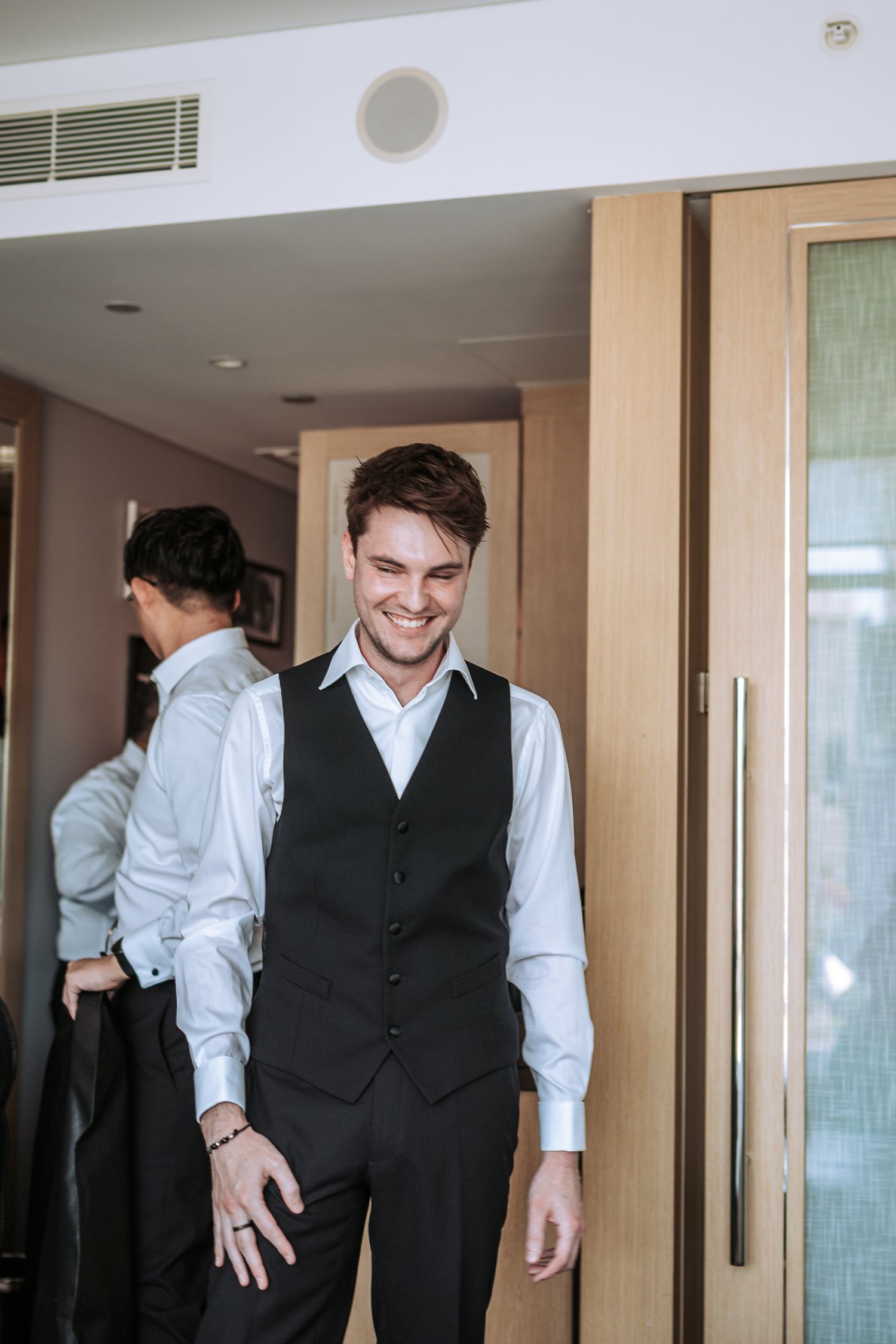 Person adjusting formal attire while getting ready in hotel room hallway.