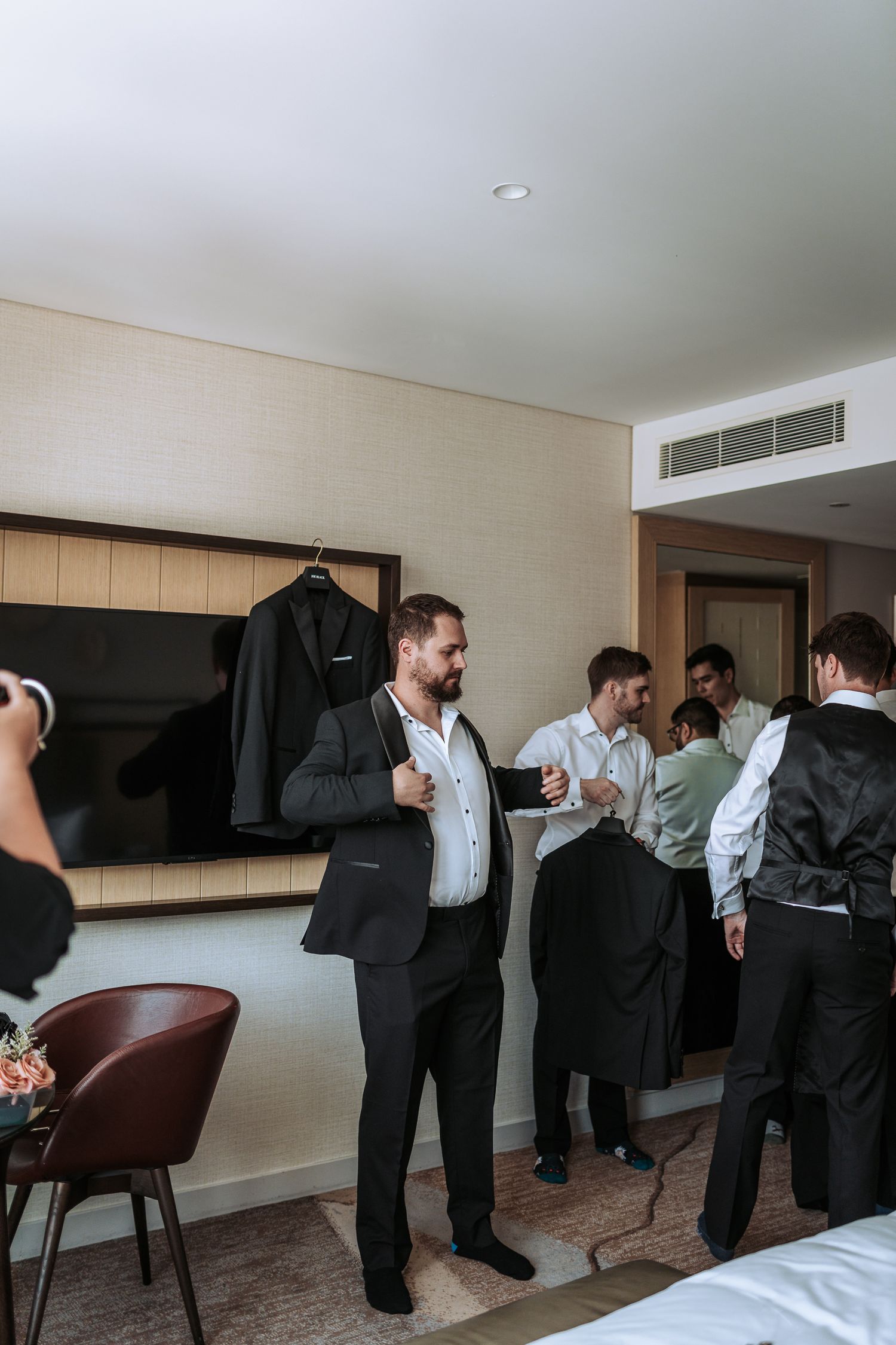 Wedding party members gathered in hotel room wearing formal attire and preparing for event.