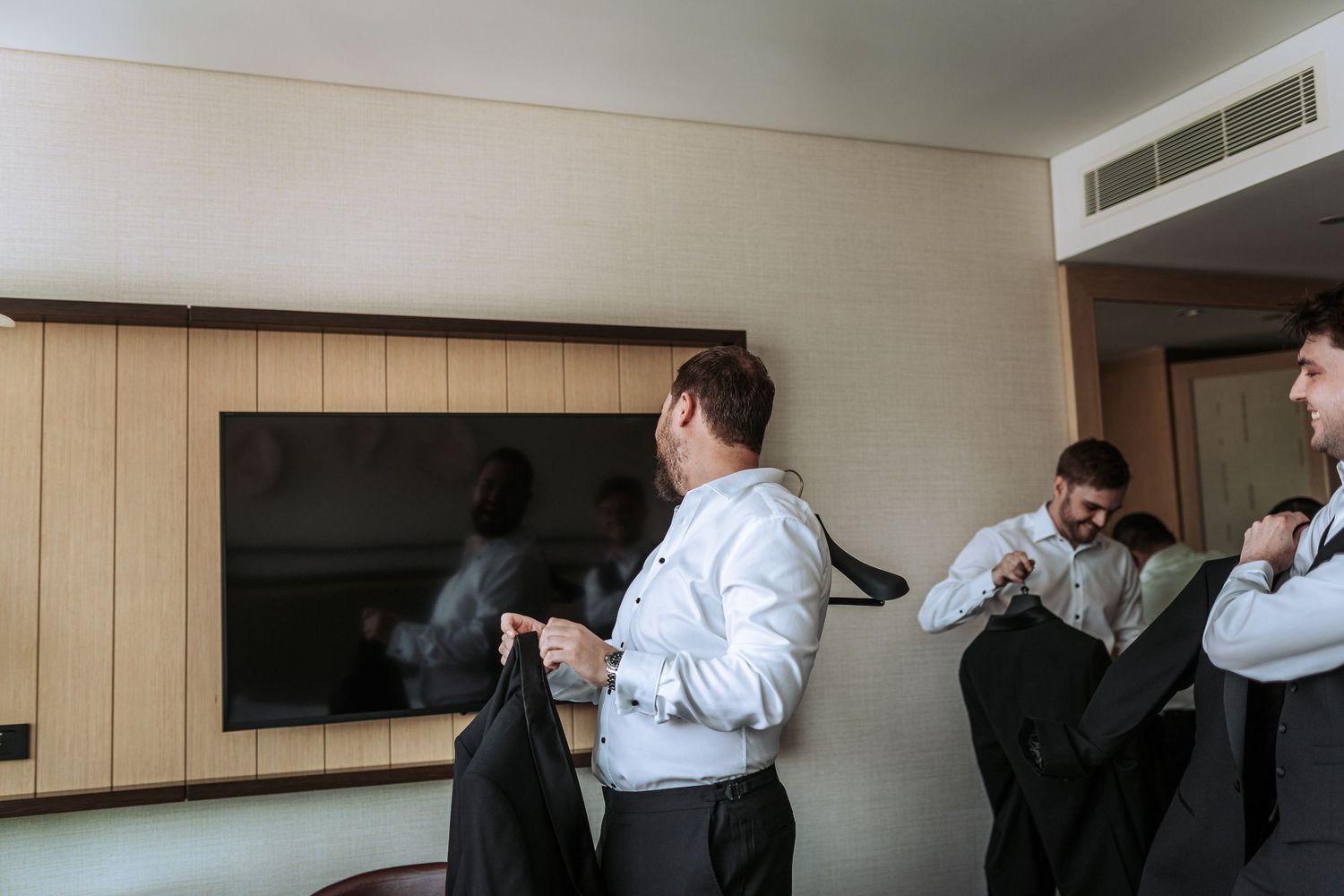 Group putting on formal jackets and getting dressed in hotel room.