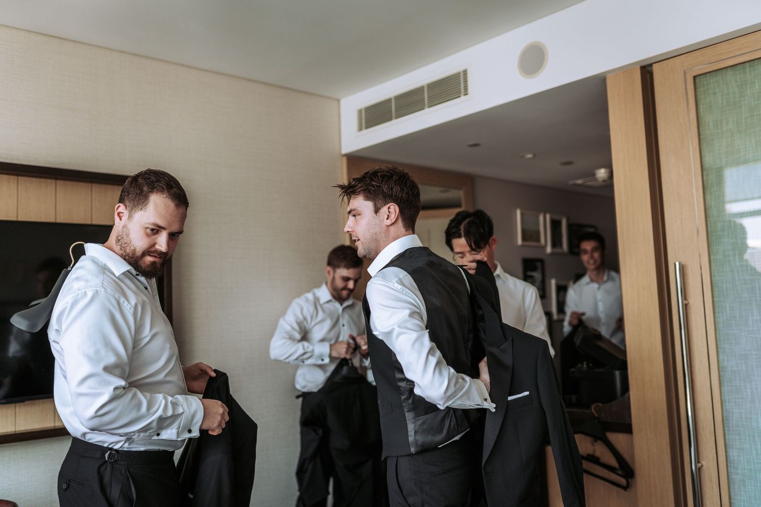 Wedding party members helping each other get dressed in formal attire.