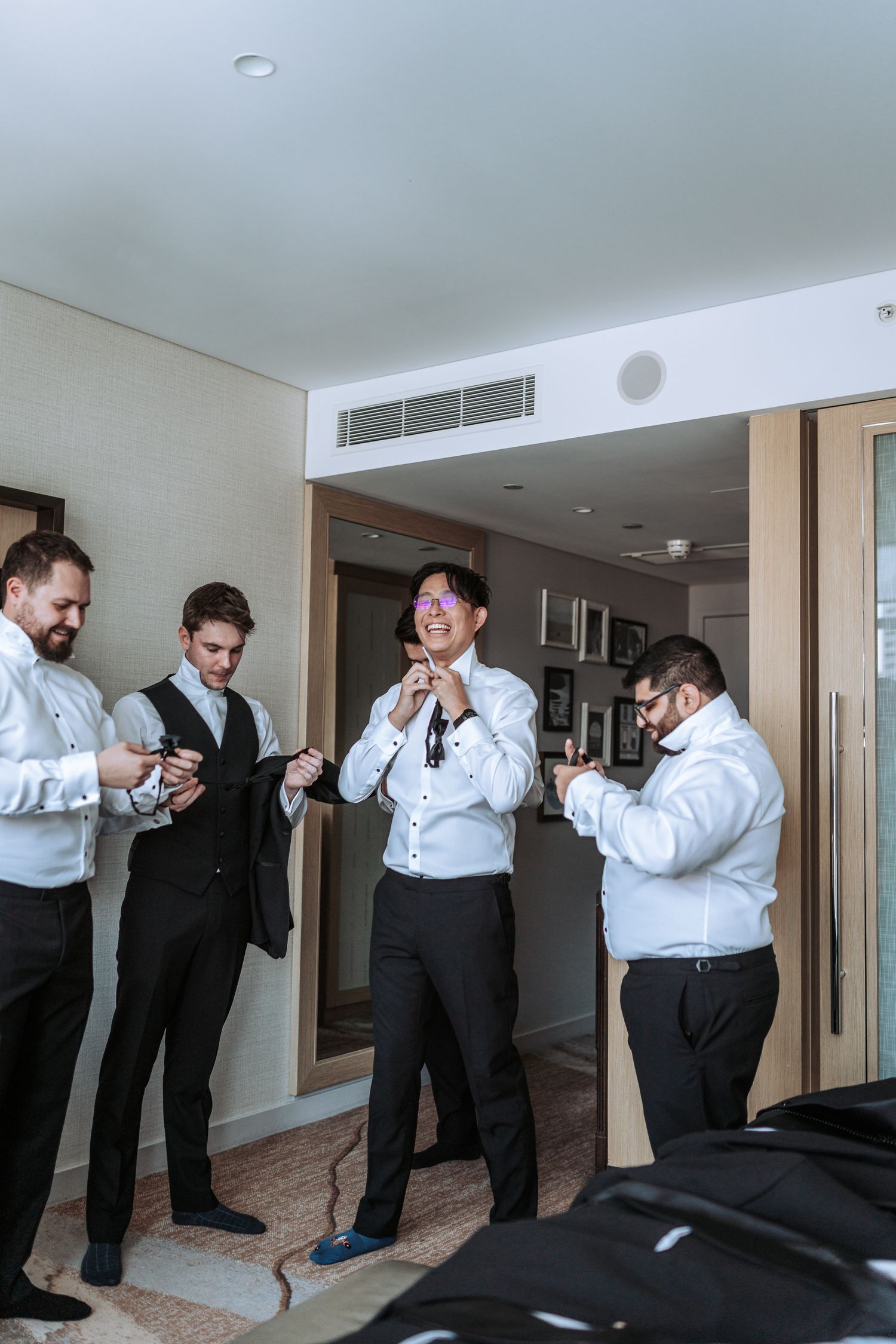 Wedding party adjusting ties and formal wear while getting ready in hotel room.