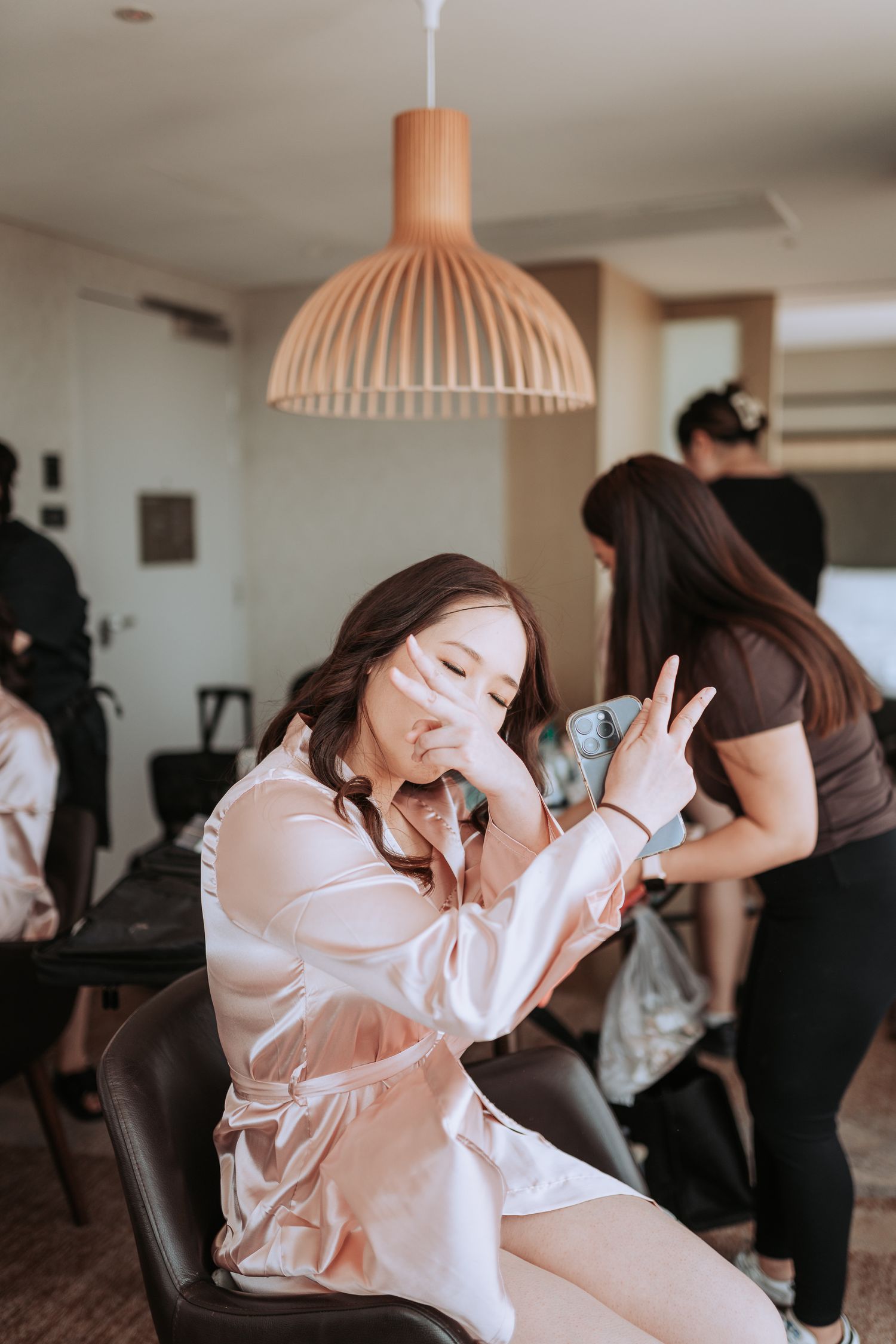 Candid moment during wedding preparations with pink-robed attendee making peace sign.