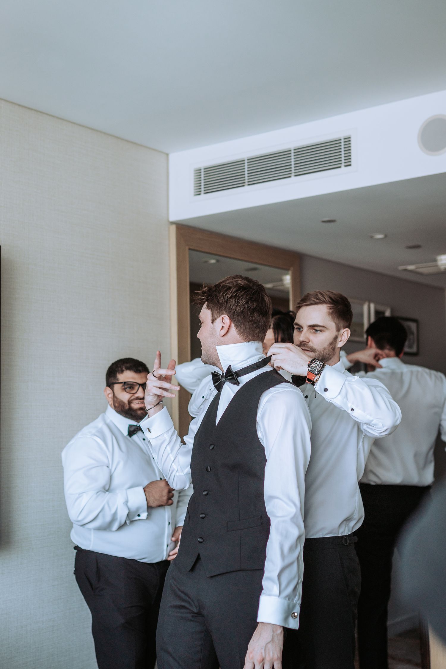Wedding party members in formal attire assist with fixing ties during pre-ceremony preparations.