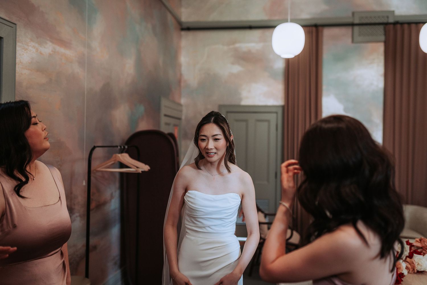 Bridal preparations in a room with dramatic cloudy wall mural and warm lighting.