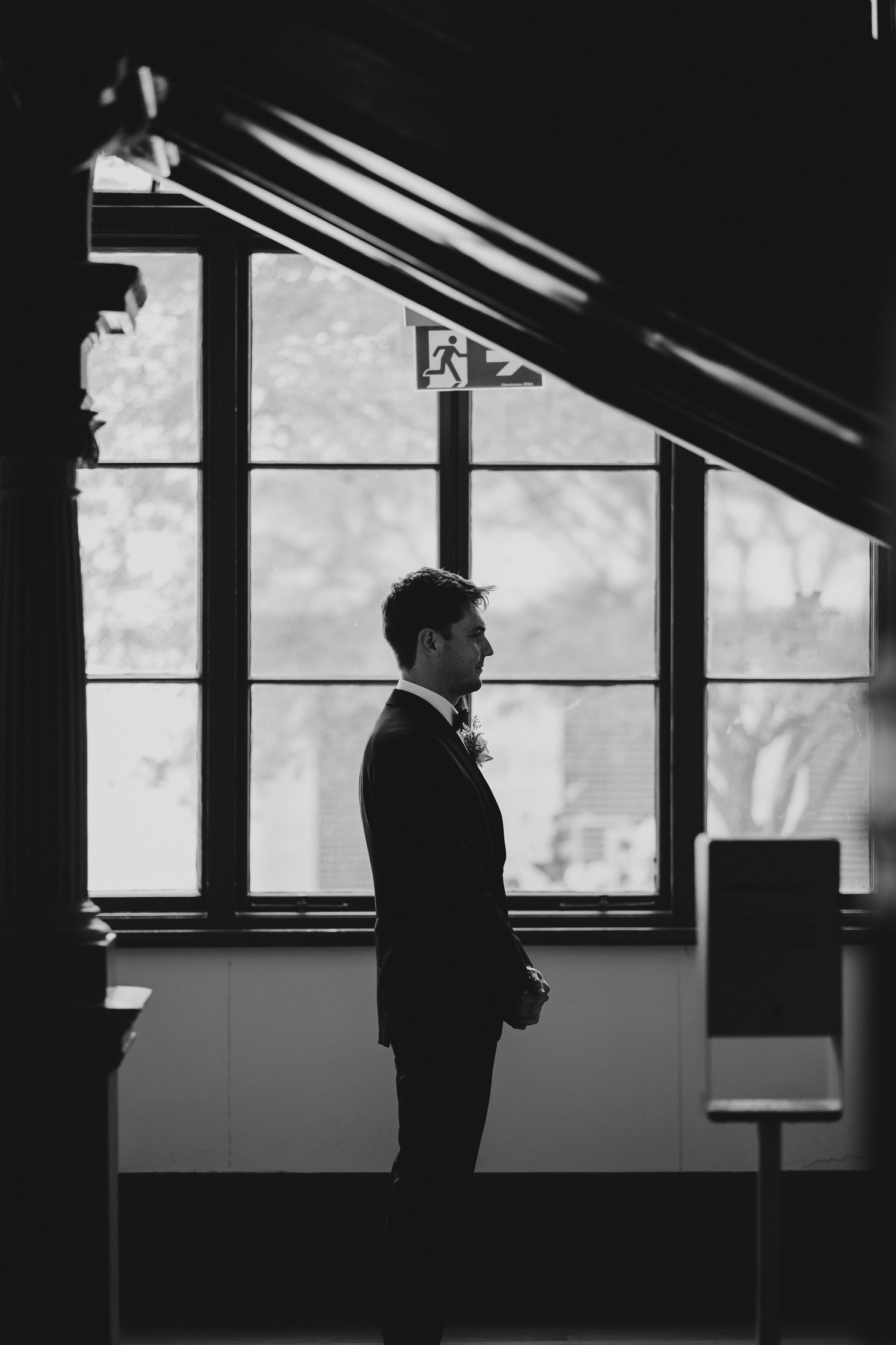 Silhouette of groom standing by large windows in formal attire.