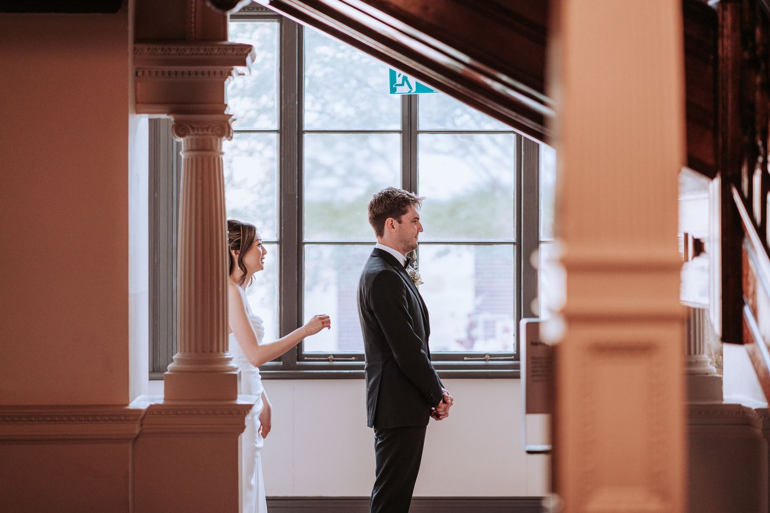 Couple standing separately by windows during first look moment at wedding.