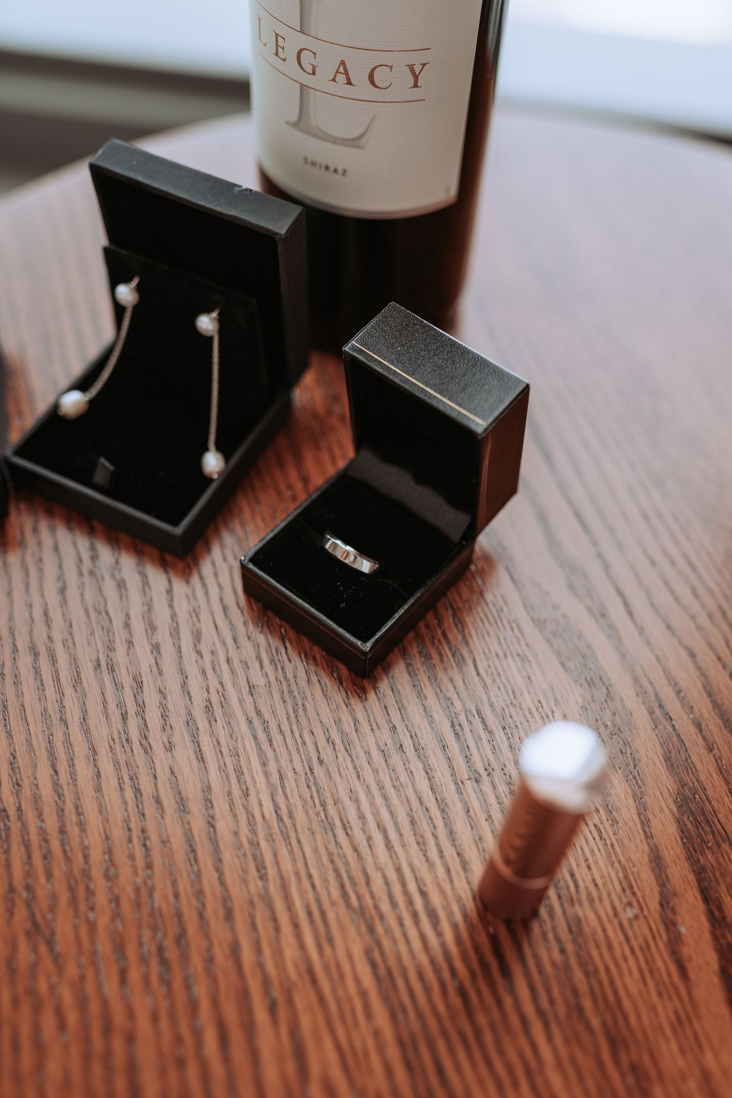 Close-up of jewelry boxes with rings and a Legacy wine bottle on a wooden table.