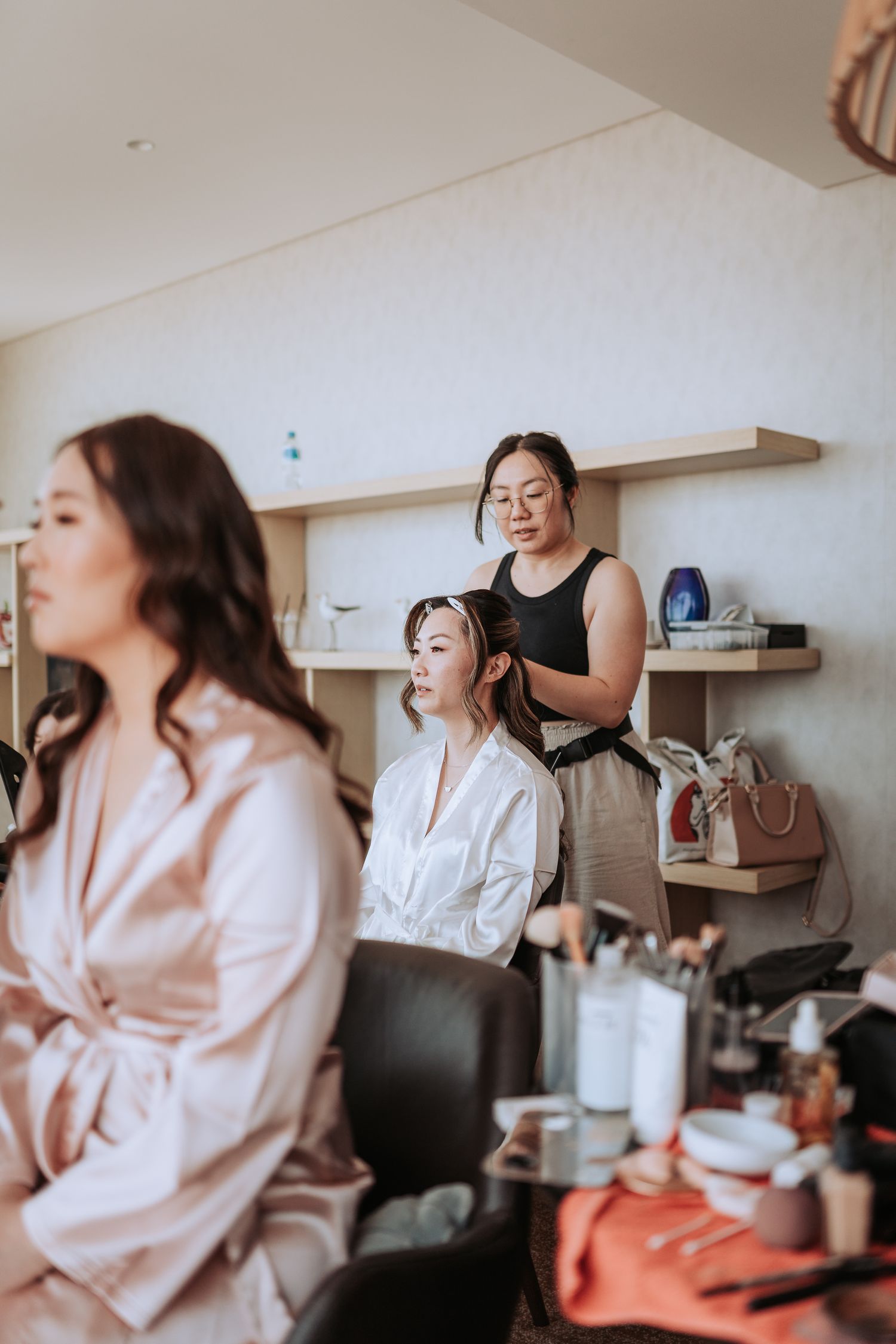 Getting ready scene with makeup artists working in a modern room with shelves.