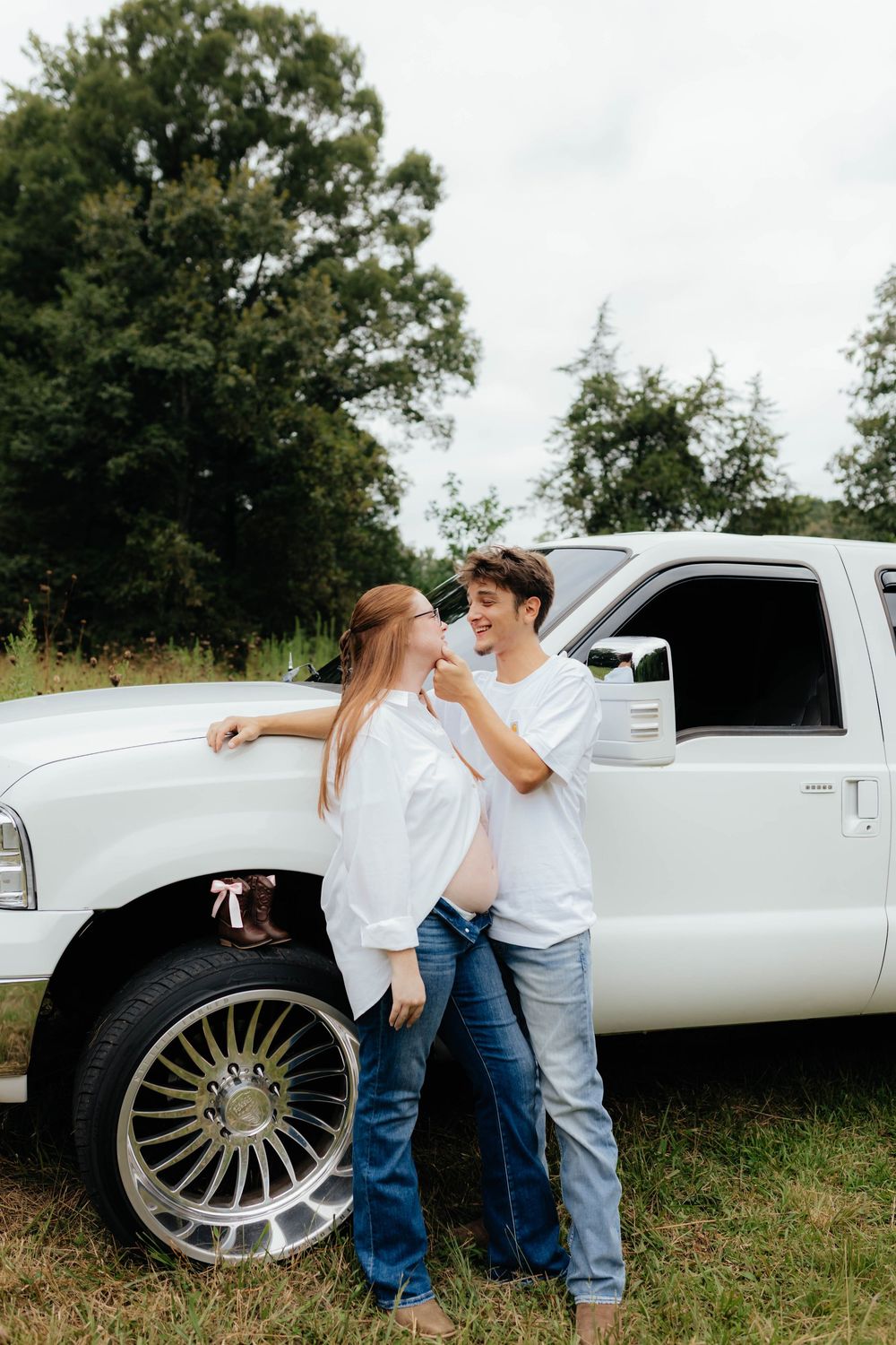 Couple poses playfully against vintage white truck during outdoor photoshoot.