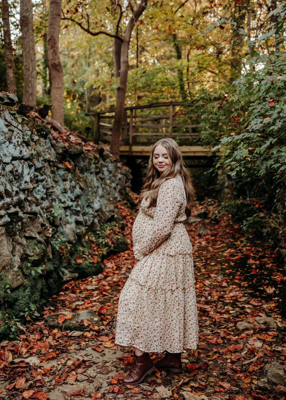Woman in flowy polka dot dress poses on wooden path surrounded by fall foliage.