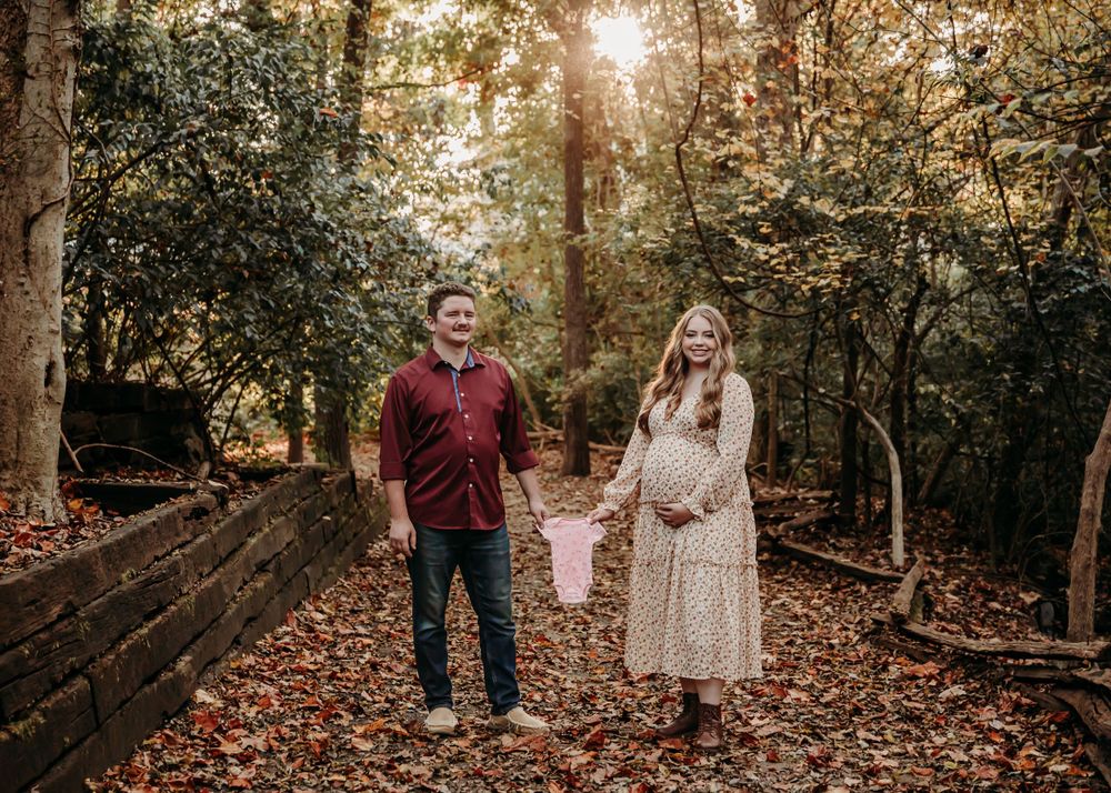 Couple walks hand in hand through wooded path covered in autumn leaves.
