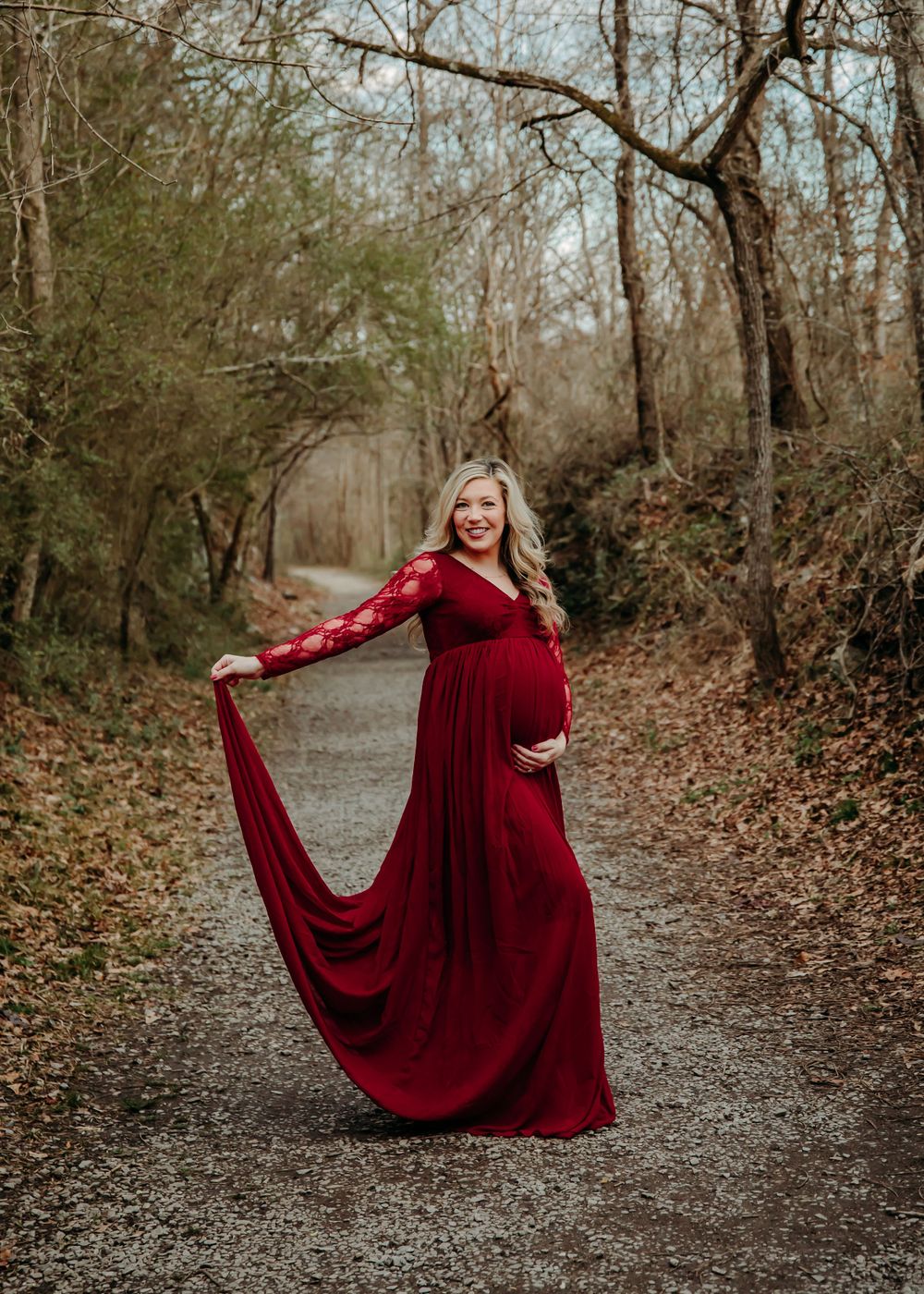 A flowing burgundy dress twirls gracefully on a wooded path during an autumn photoshoot.
