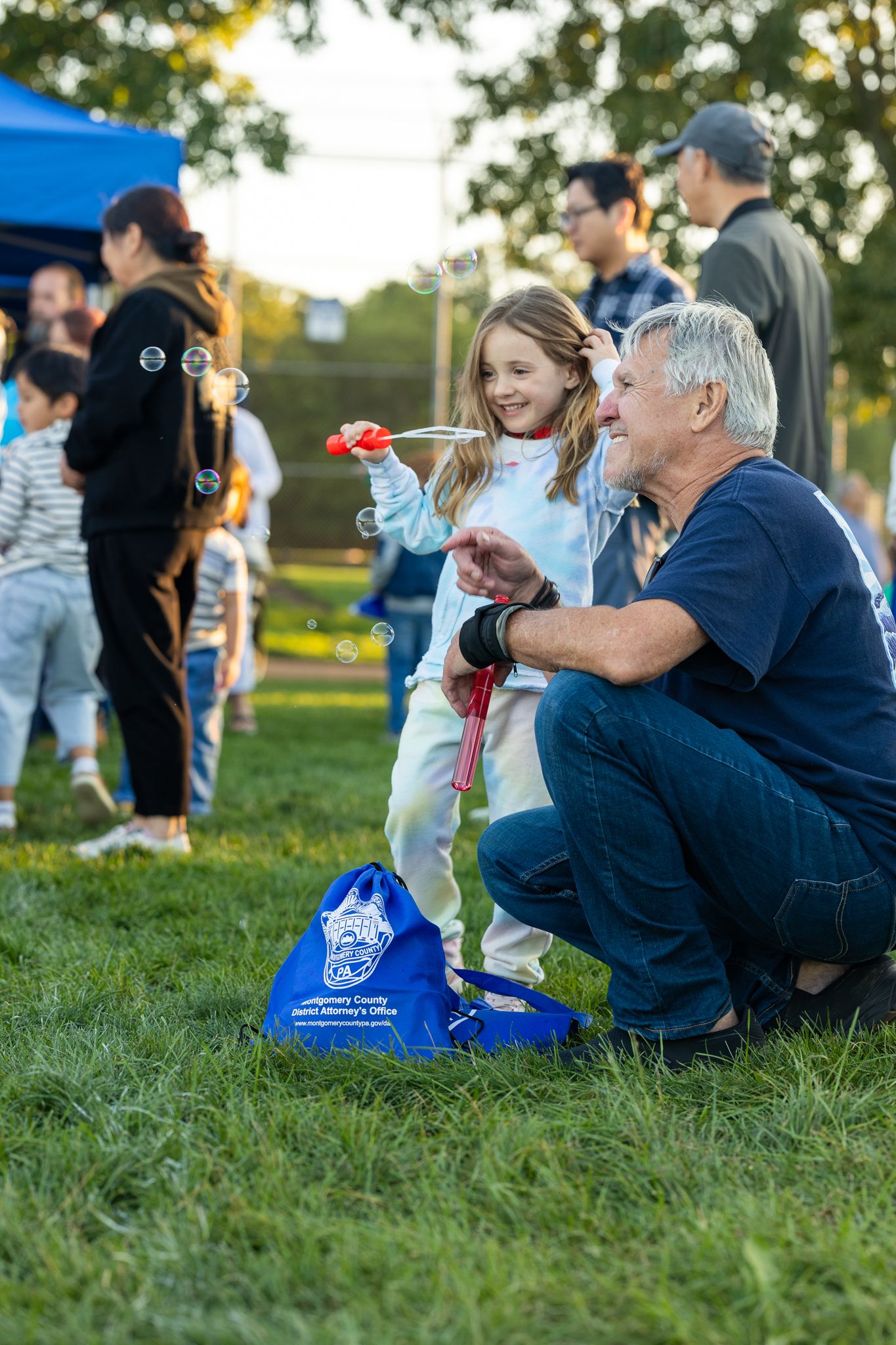Family enjoying outdoor activities at community event with blue tent in background.