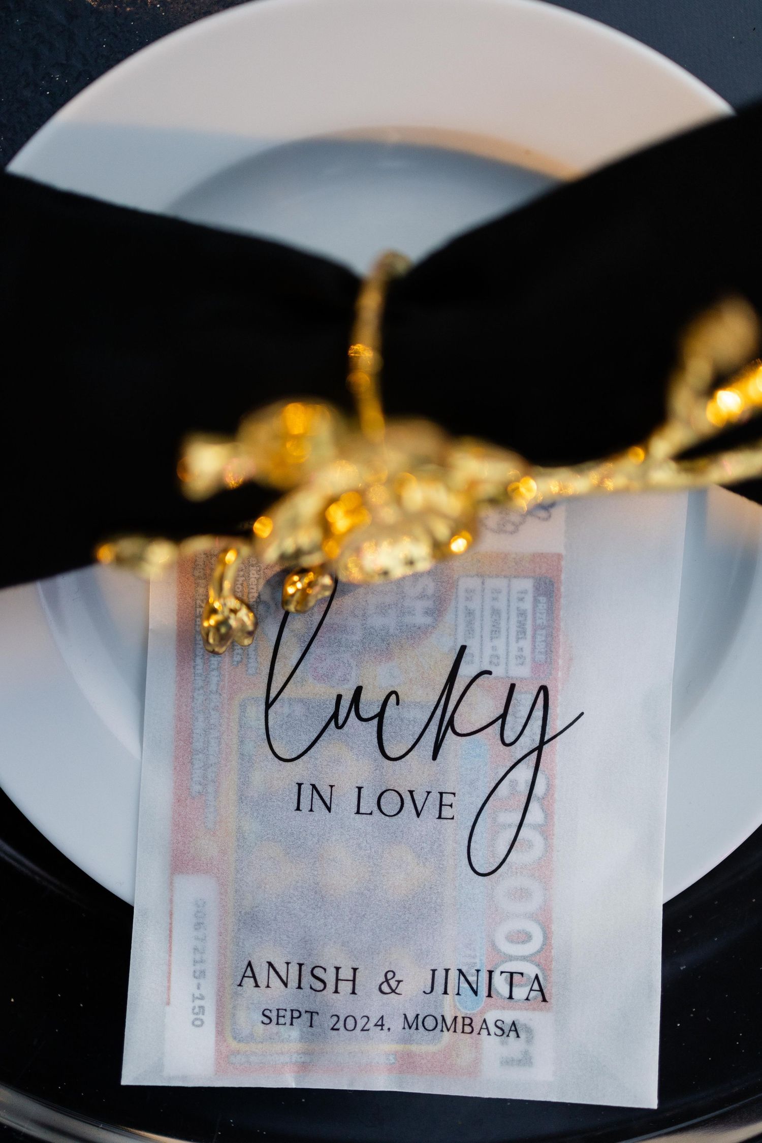 Lucky in Love wedding favor card for Anish & Jinita, Sept 2024 Mombasa, displayed on black plate with gold decor.