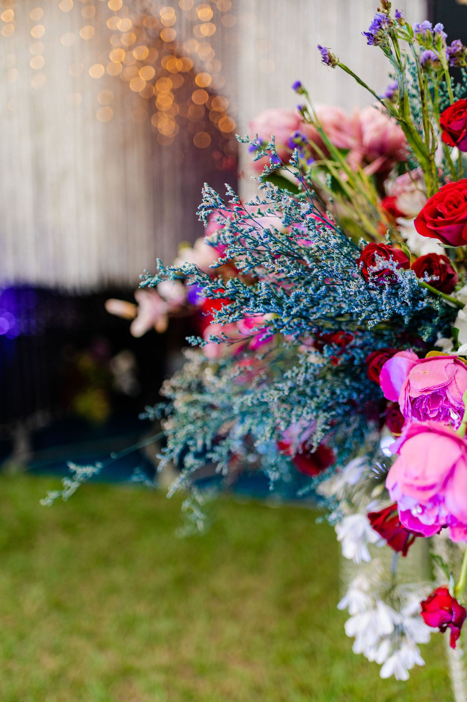 Vibrant floral arrangement with pink, red roses and blue foliage against bokeh lights backdrop.