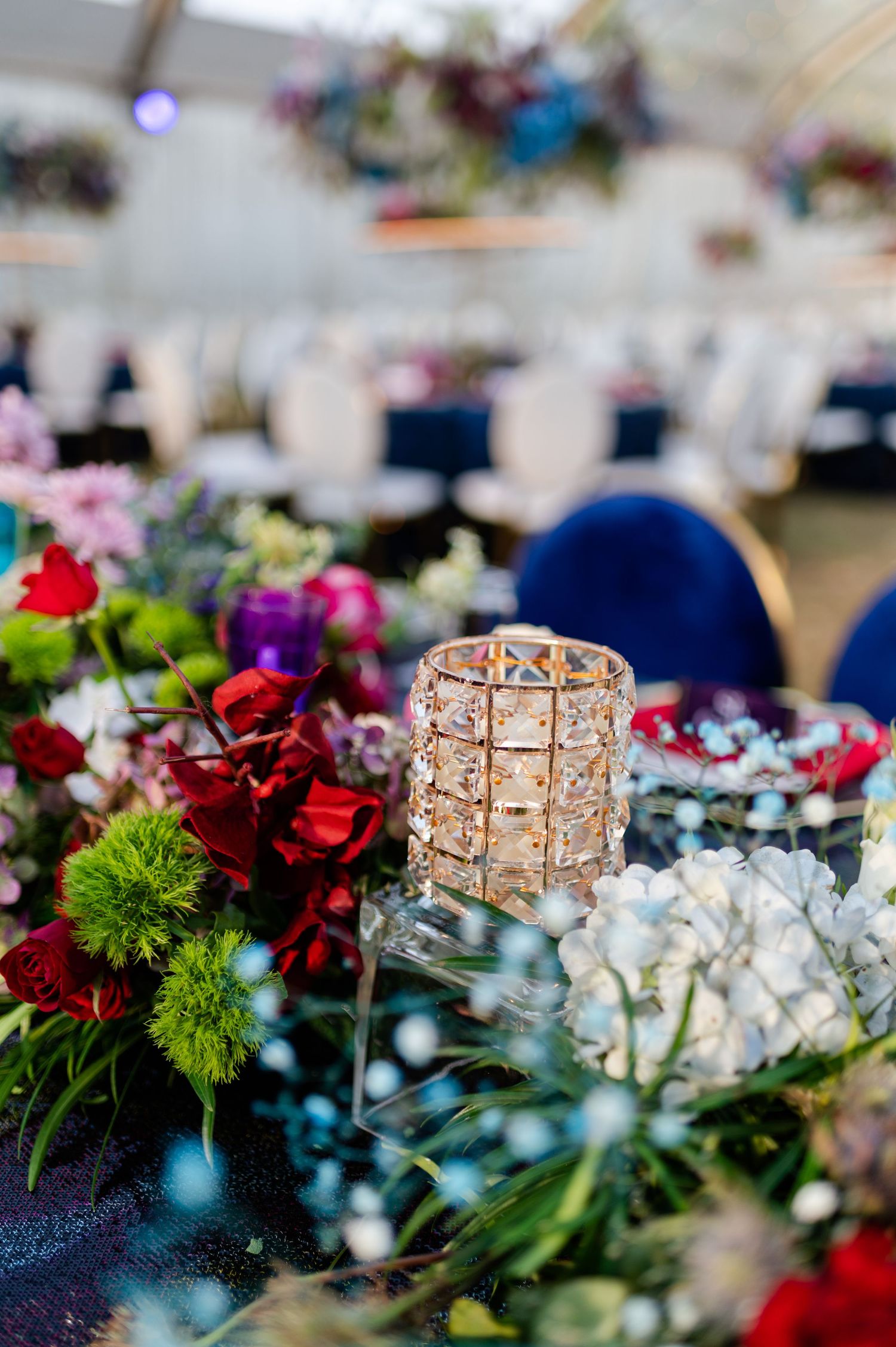 Crystal candle holder surrounded by colorful wedding centerpiece flowers including red roses, green blooms, and white hydrangeas.