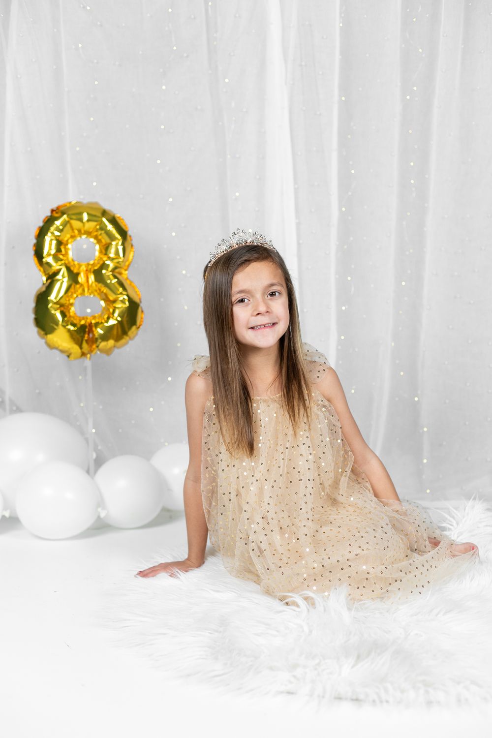 Birthday scene with child in sparkly dress and number 8 balloon against white backdrop.