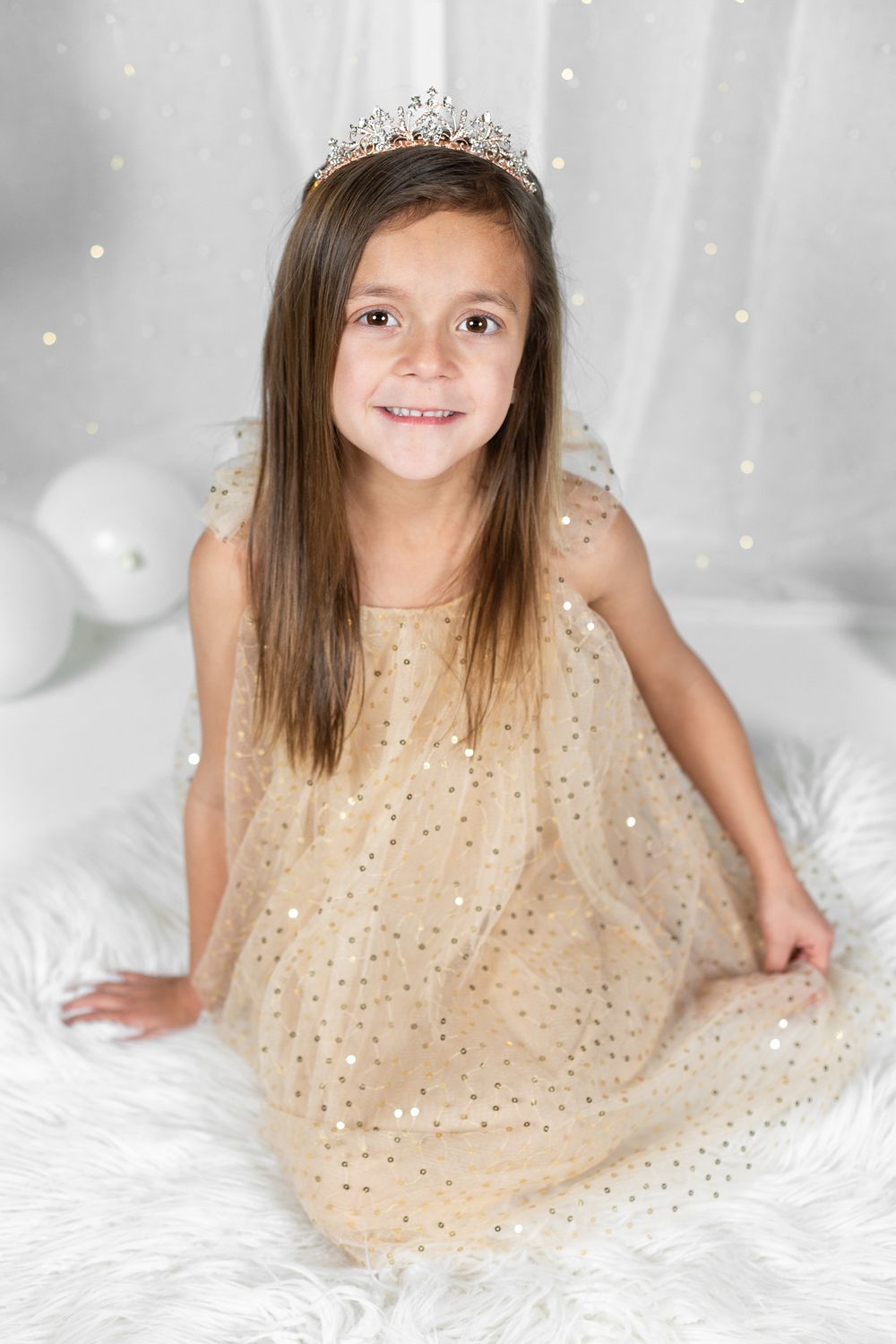 Festive portrait with sparkly dress and tiara against white background with balloons.