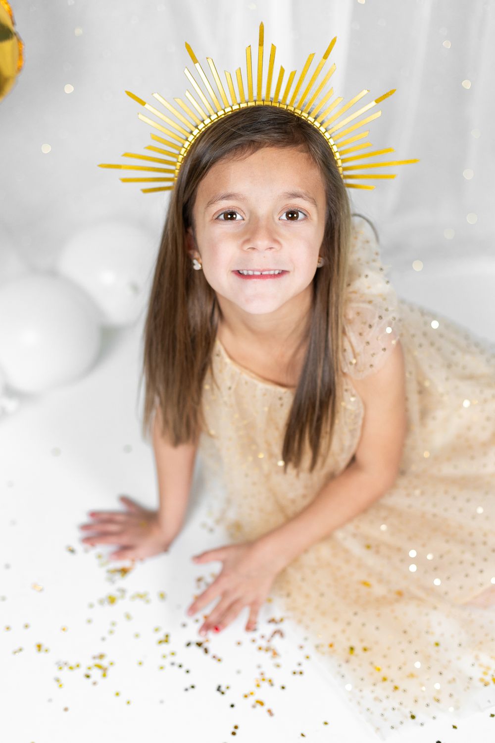 Portrait with sunburst crown and sparkly dress against white backdrop with gold accents.