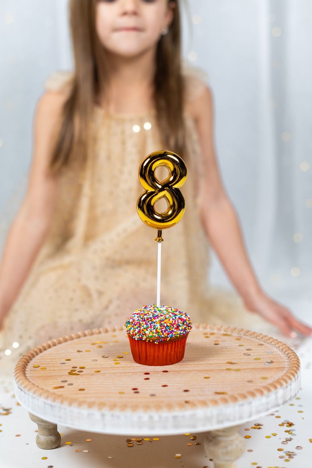 Gold number 8 birthday candle on decorated cupcake sitting on ornate white cake stand.