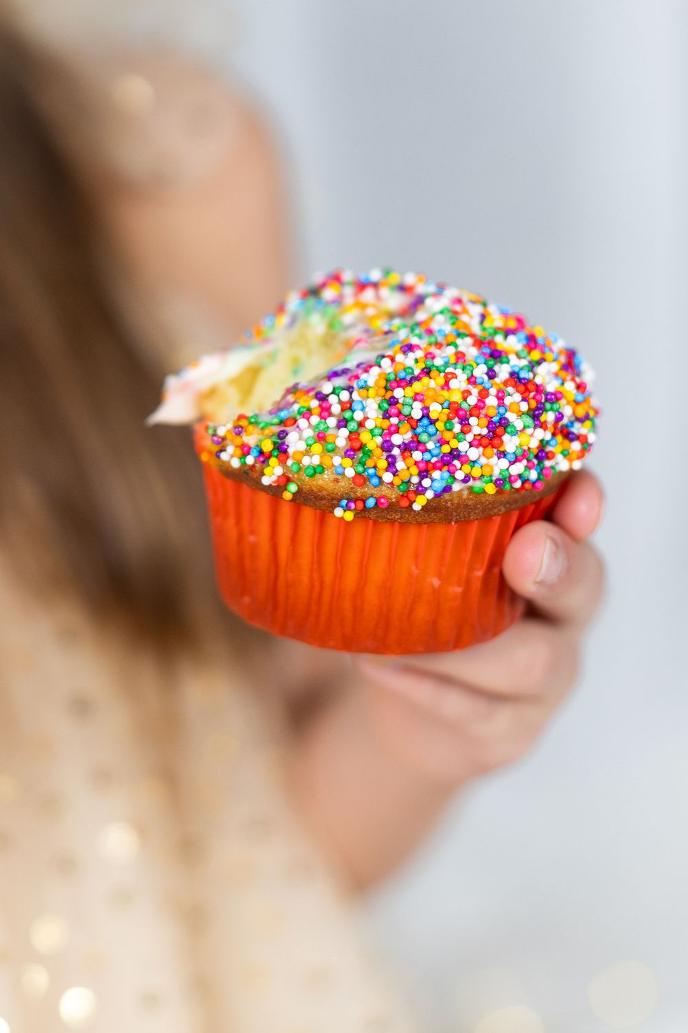 Close-up of colorful sprinkle-covered cupcake being held against sparkly background.