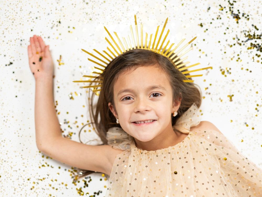 Smiling child with gold sunburst crown lying amid scattered glitter confetti.