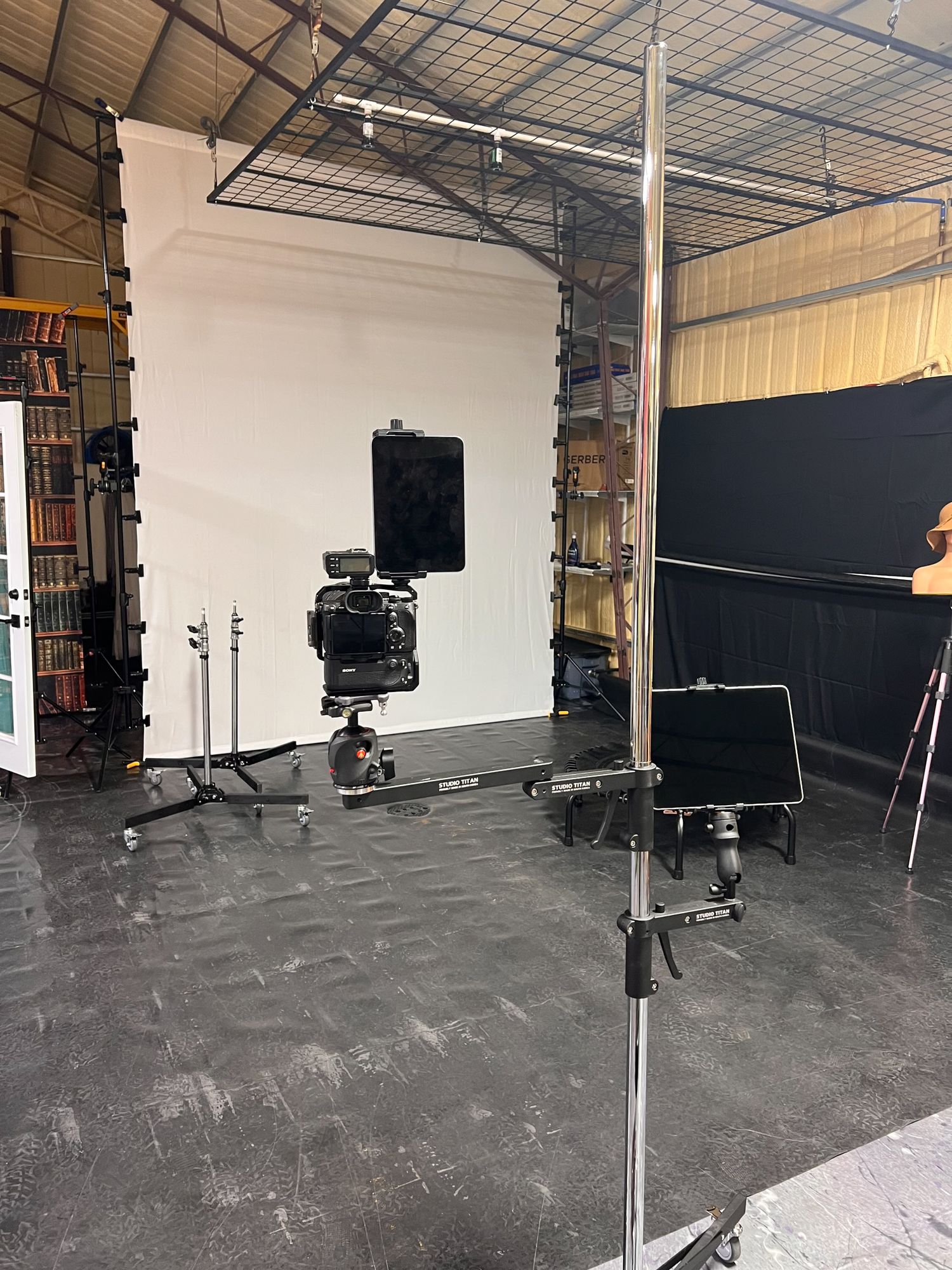 Professional photography studio with white backdrop, camera equipment, and lighting stands on concrete floor.
