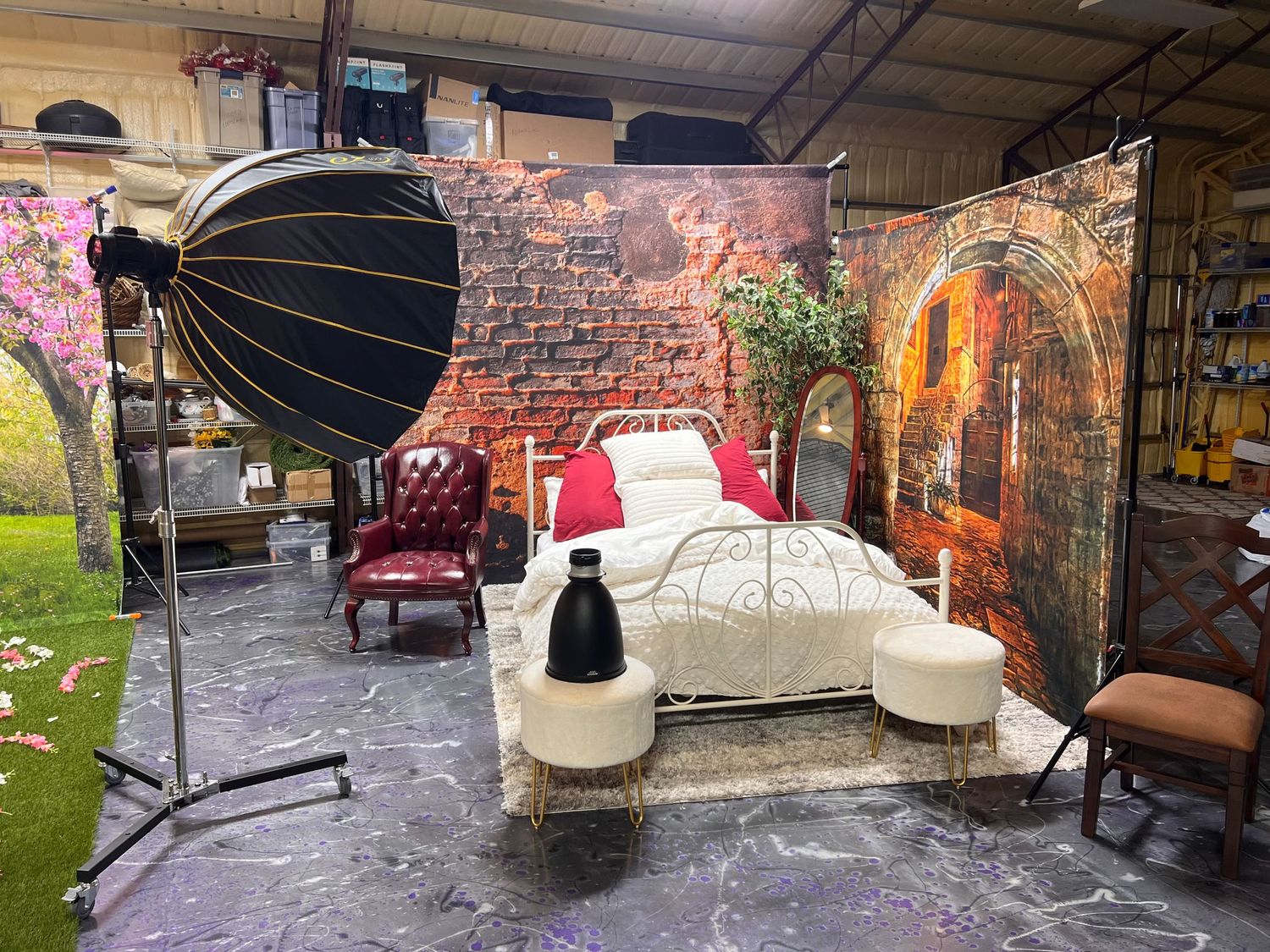 Bedroom photography set with vintage brick backdrop, white bed, and professional lighting equipment.