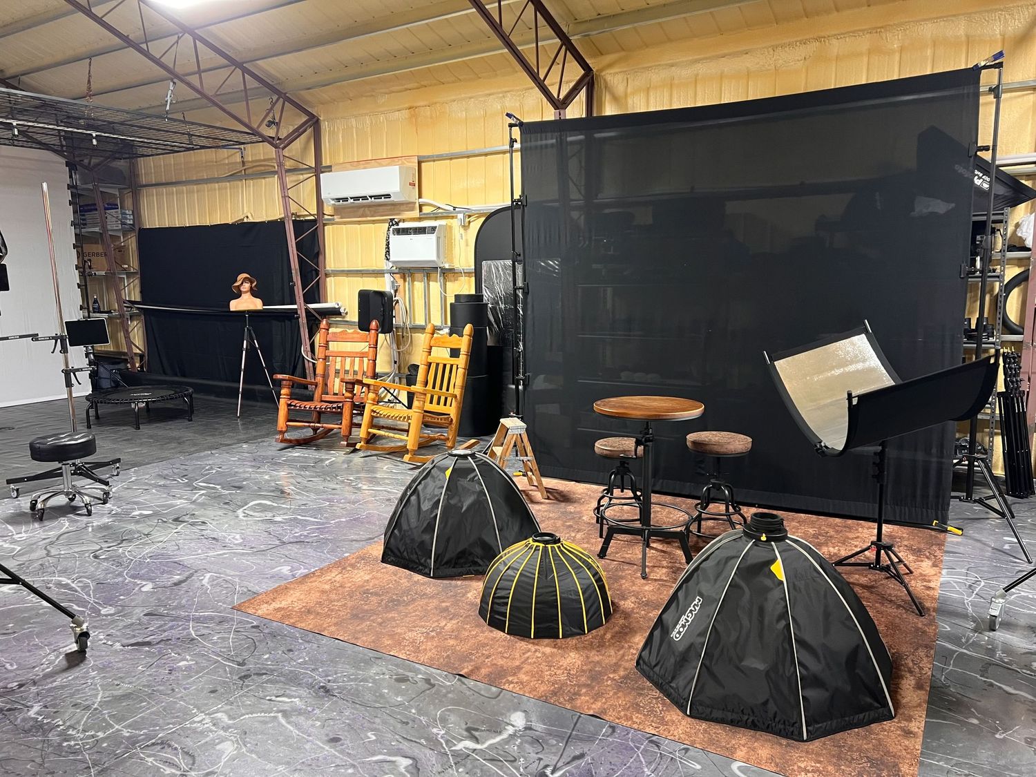 Photography studio with black backdrop, wooden chairs, and professional lighting equipment on orange carpet.