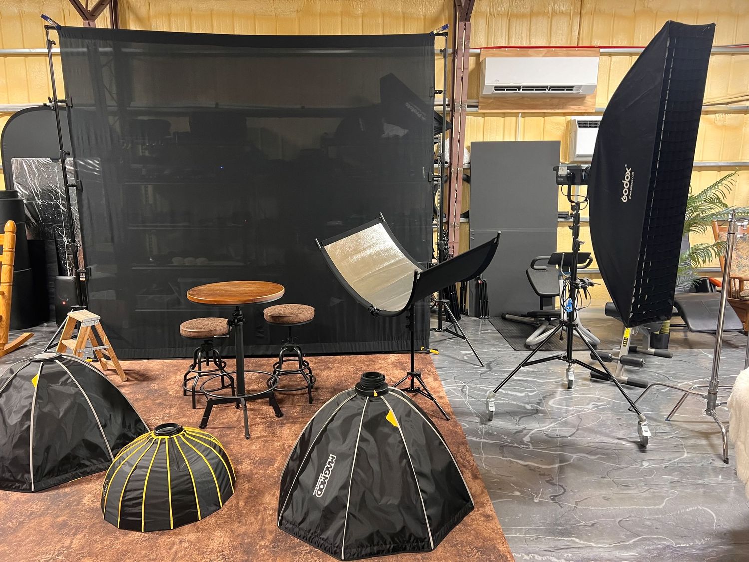 Professional photography studio setup with black backdrop, lighting equipment, and reflectors on concrete floor.