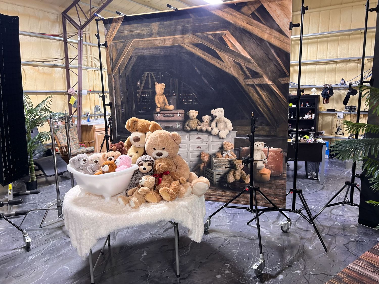 Photography studio setup with collection of teddy bears arranged on white table against dark backdrop.