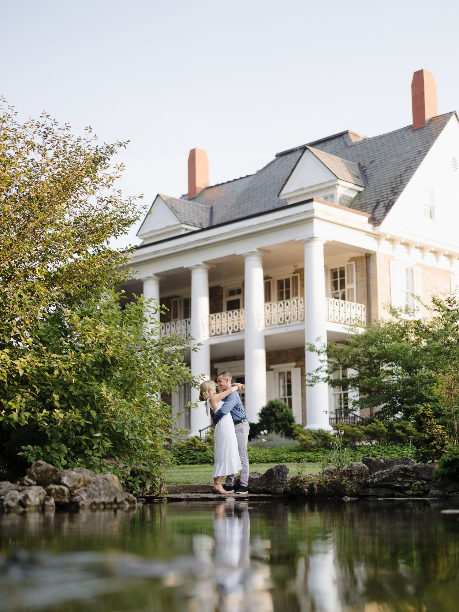 An elegant southern style mansion with white columns and a reflecting pond creates a dreamy wedding venue setting.