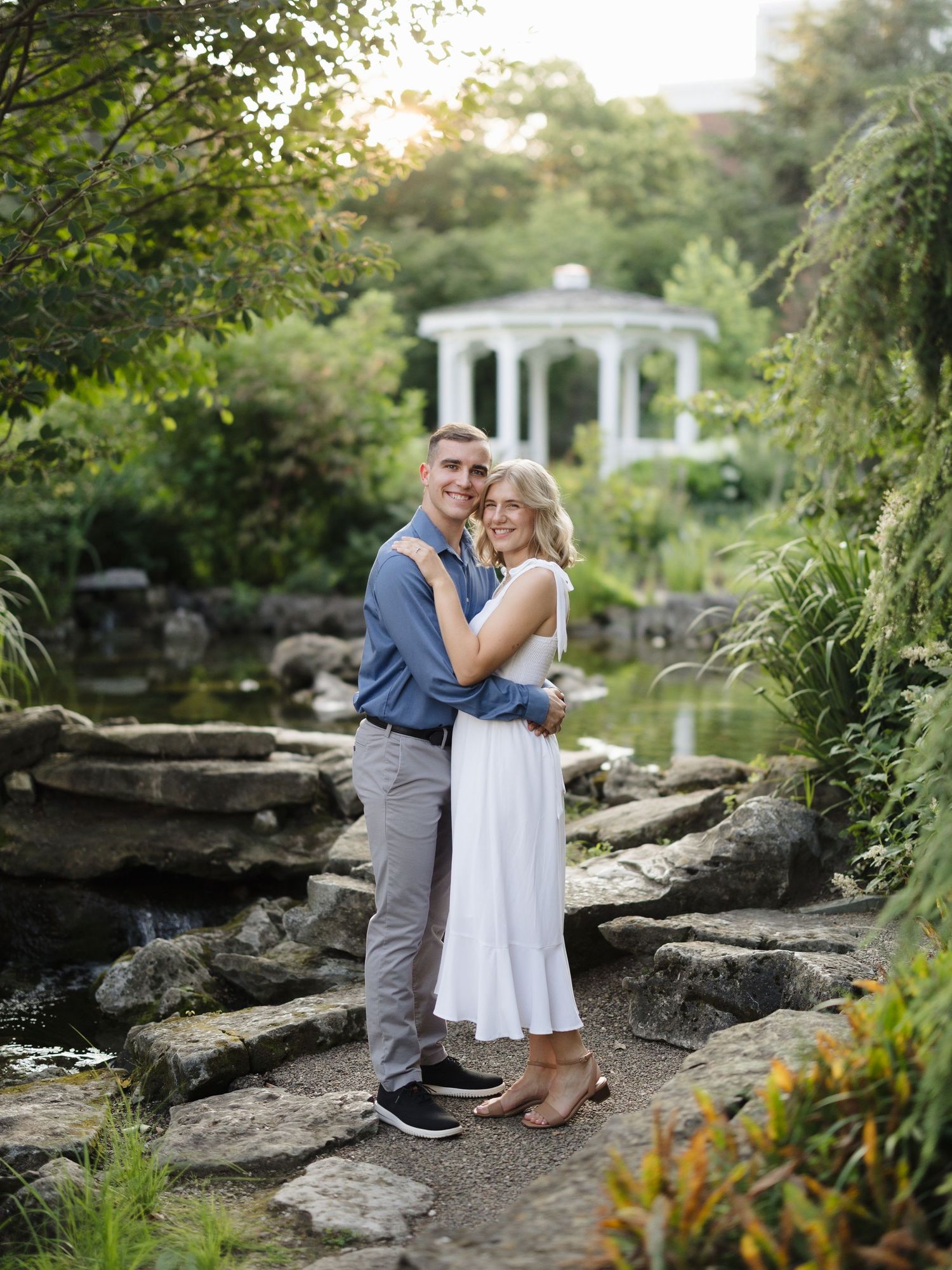 A couple shares a romantic moment together while sitting on natural stone steps in a lush garden setting at golden hour.