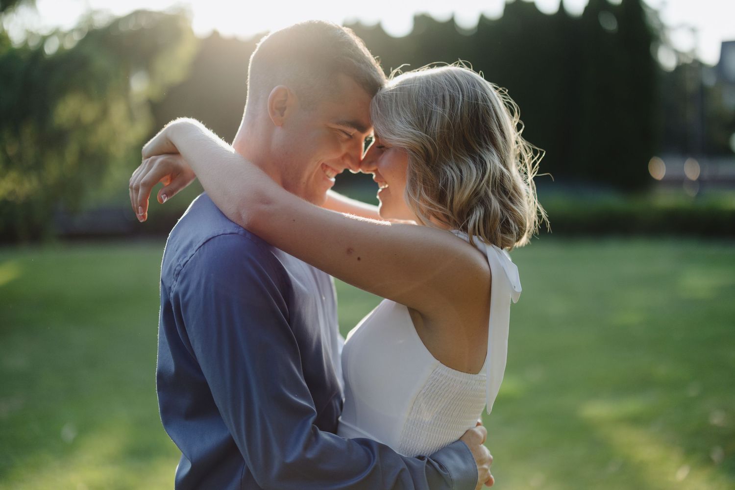 A romantic moment between a couple in formal wedding attire embracing outdoors in a sunlit garden setting.