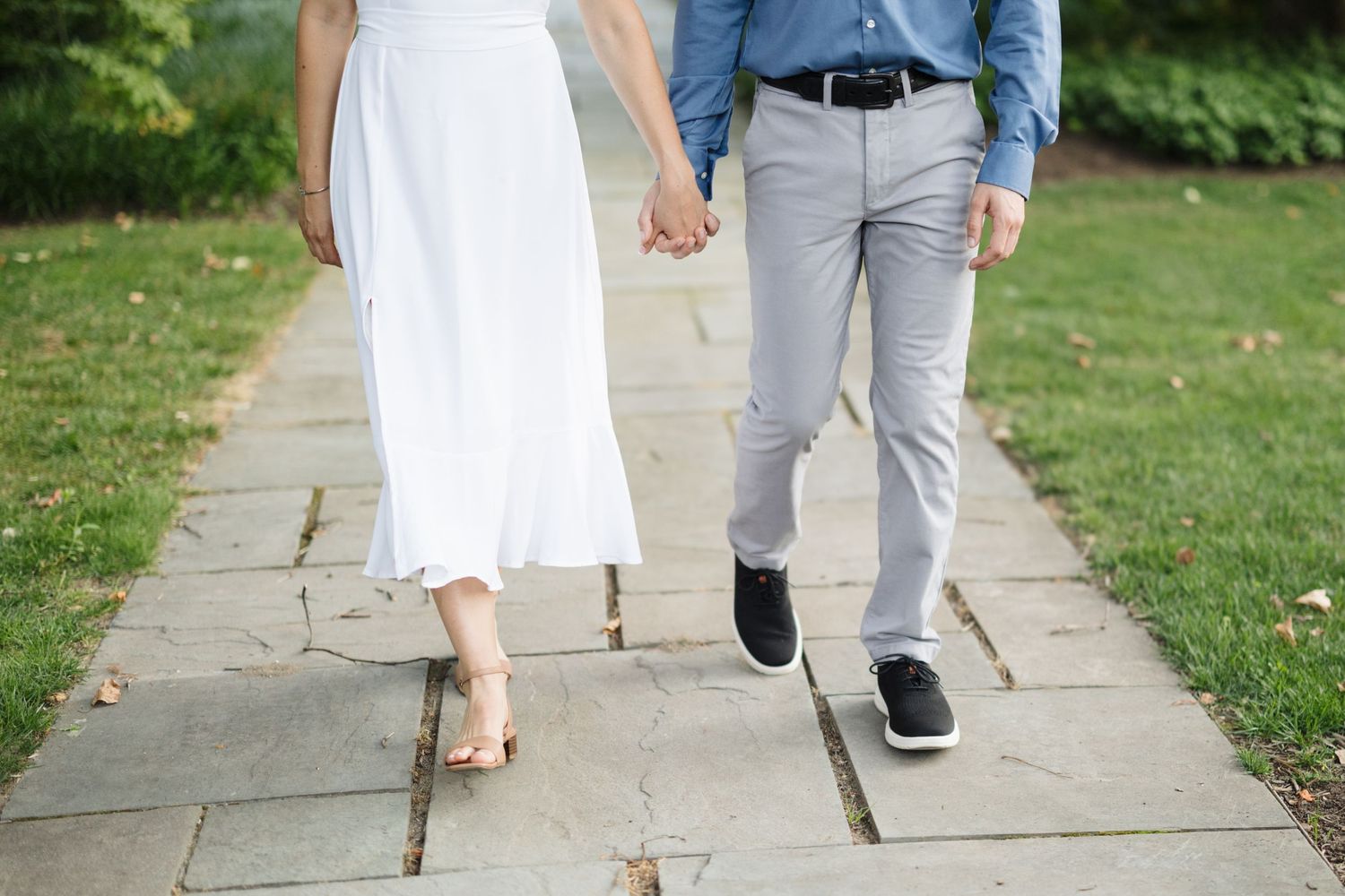 Couple walking together on stone path with woman in white dress and man in gray pants and blue shirt.