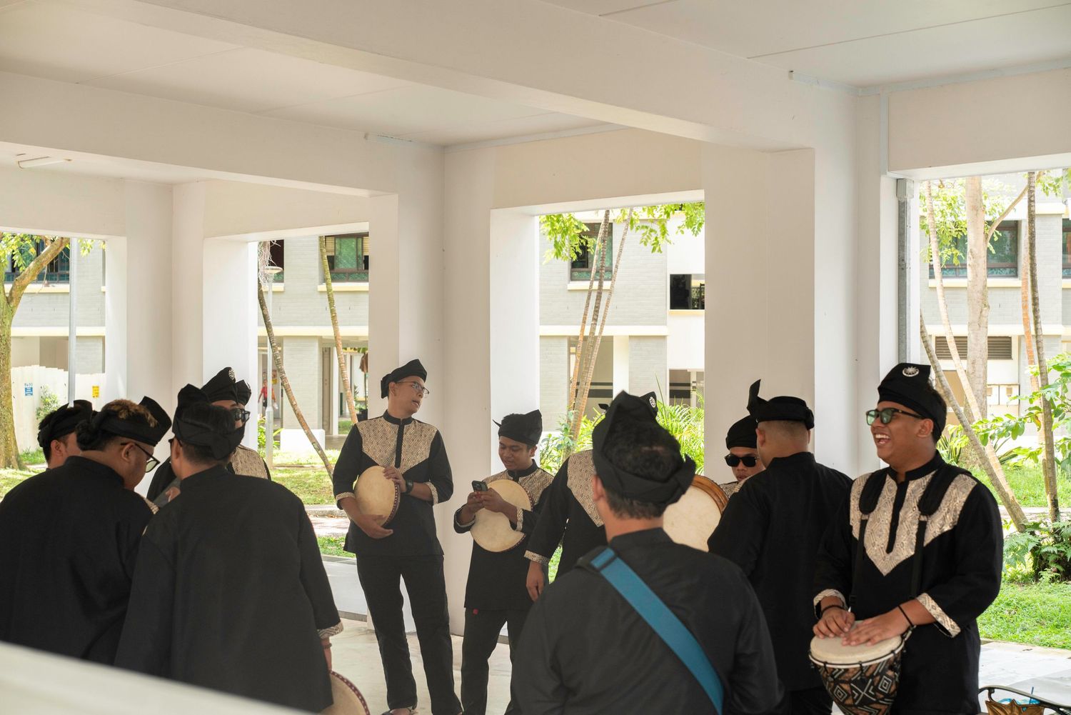 A group gathers inside a bright white room with large windows overlooking a tropical garden.