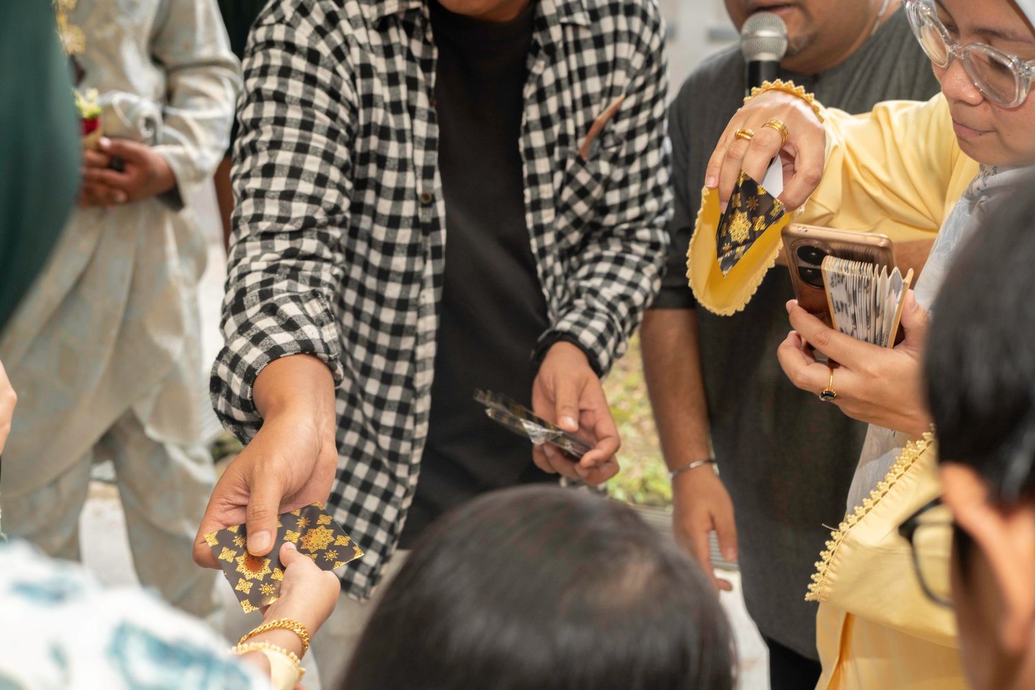 People gathering around as a person in a checkered shirt and another in yellow pour drinks into a glass.