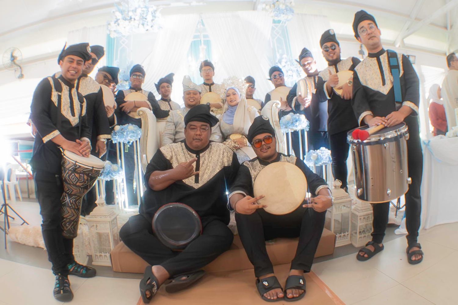 Traditional folk music ensemble performs with drums and tambourines in a bright indoor venue wearing cultural attire.