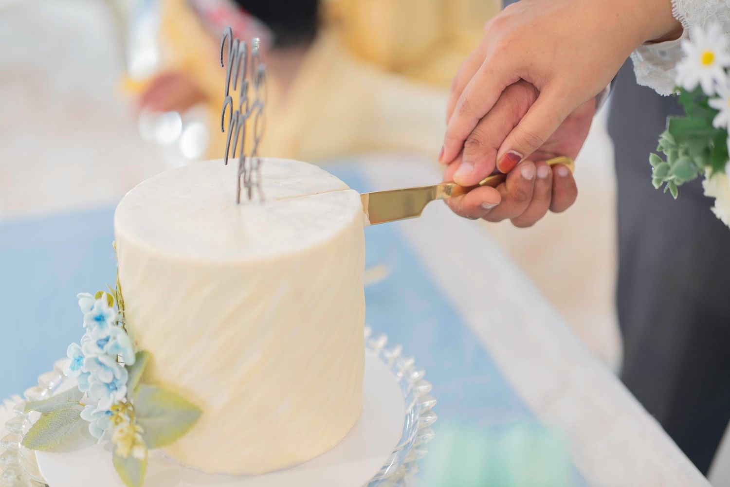 Newlyweds cutting into an elegant white wedding cake decorated with delicate floral accents.