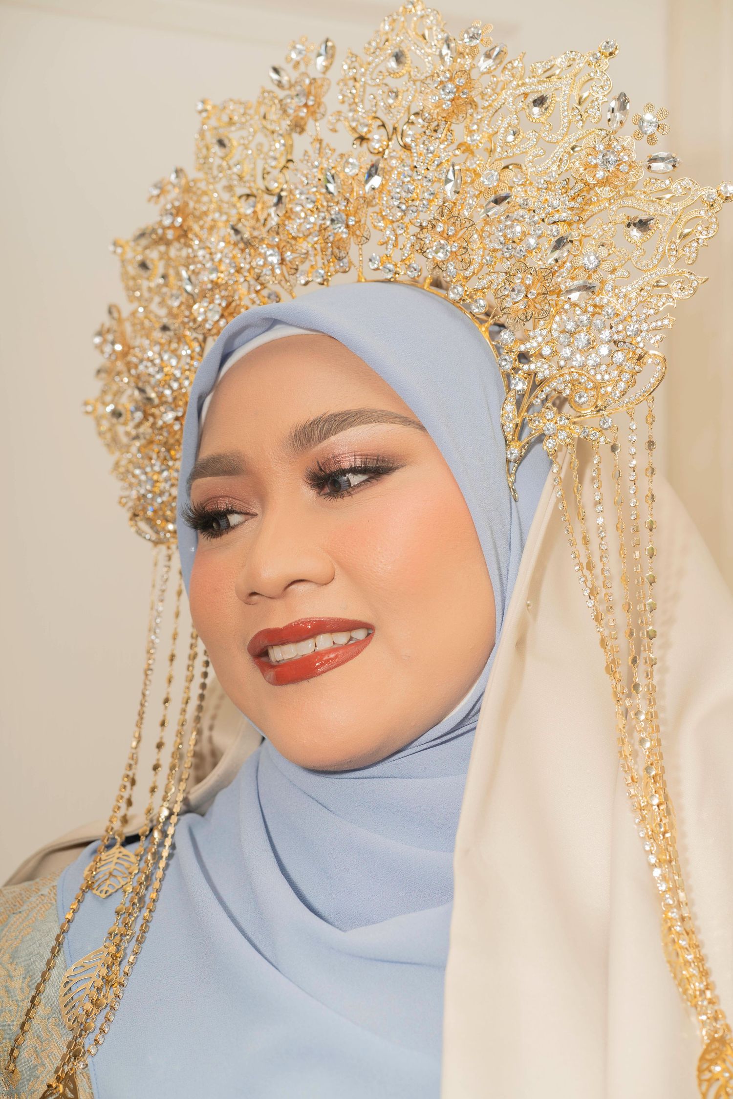 A person wearing a powder blue hijab and elegant golden crown headpiece with dramatic makeup.