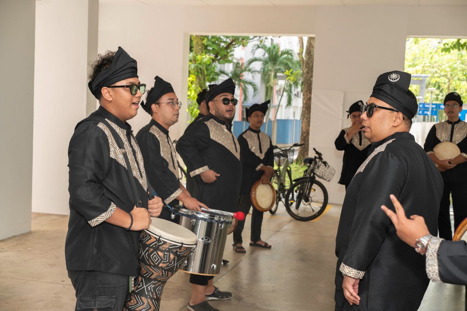 A line of people in black clothing and hats stand in front of a white wall at an indoor venue or gallery space.