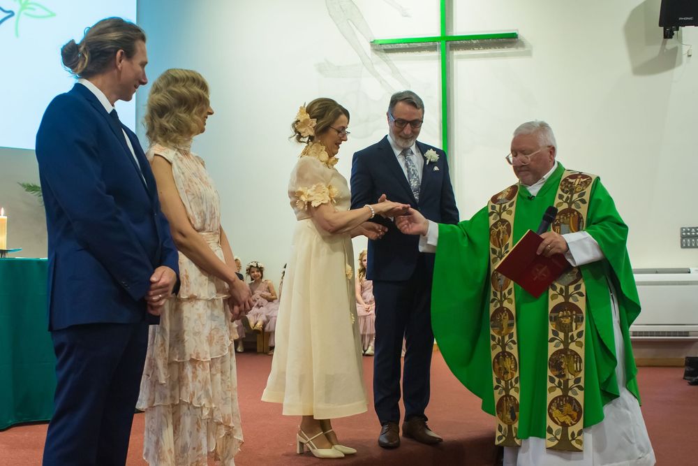 A priest in green robes performs a Catholic wedding ceremony for a couple in a church setting.