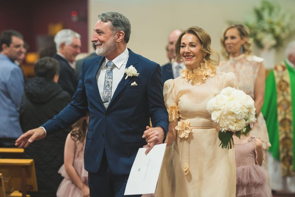 A couple celebrates during their wedding ceremony in a church while holding hands and carrying a white bouquet.