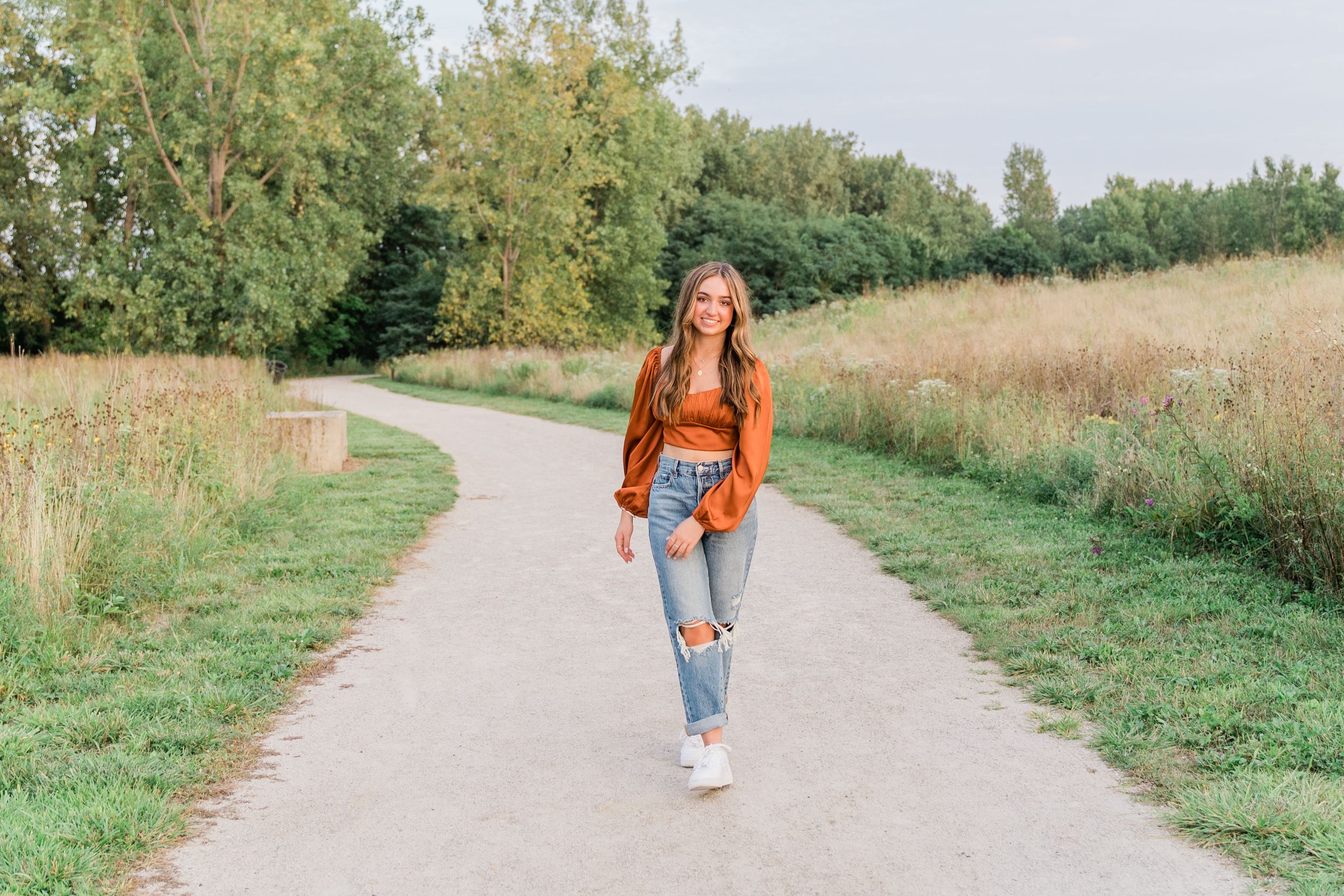 Person in orange sweater walking down a rural gravel path during autumn.